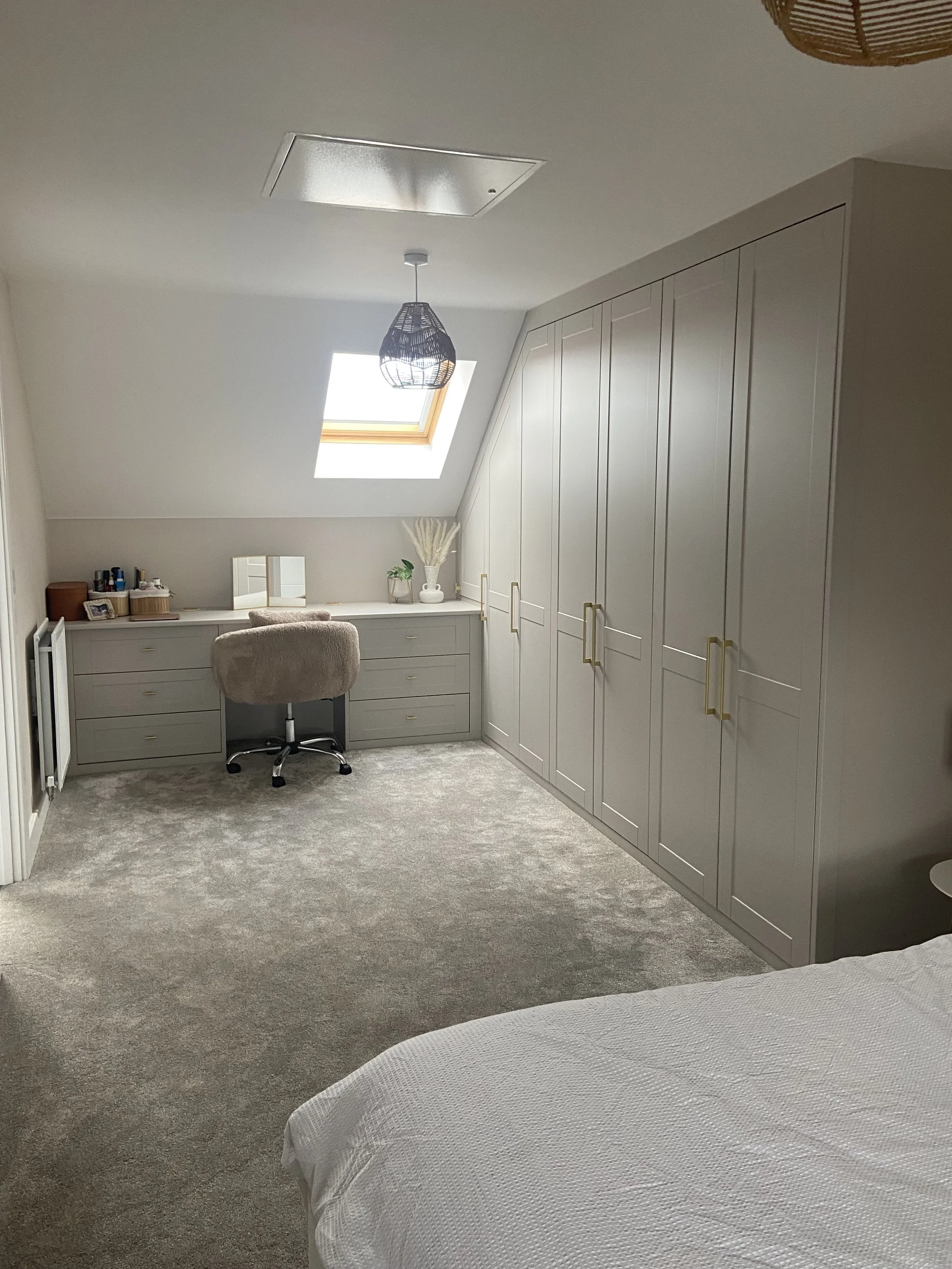 A cozy bedroom with a large built-in closet, a skylight window, and a vanity area with a chair and decorative items, illuminated by natural light.