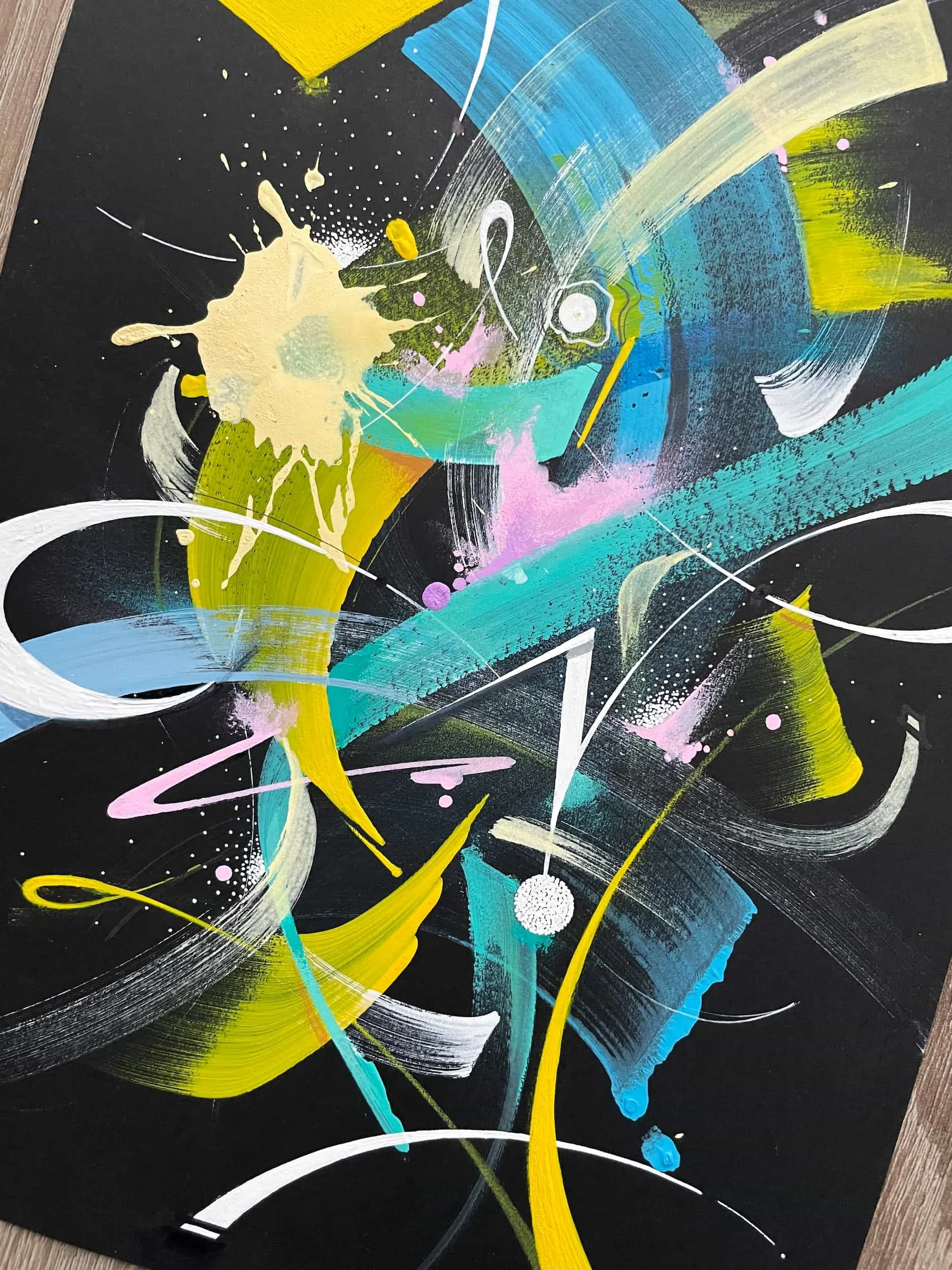 Abstract painting with vibrant splashes of yellow, pink, blue, white, and green on a black background, featuring swirling lines, splatters, and brushstrokes.