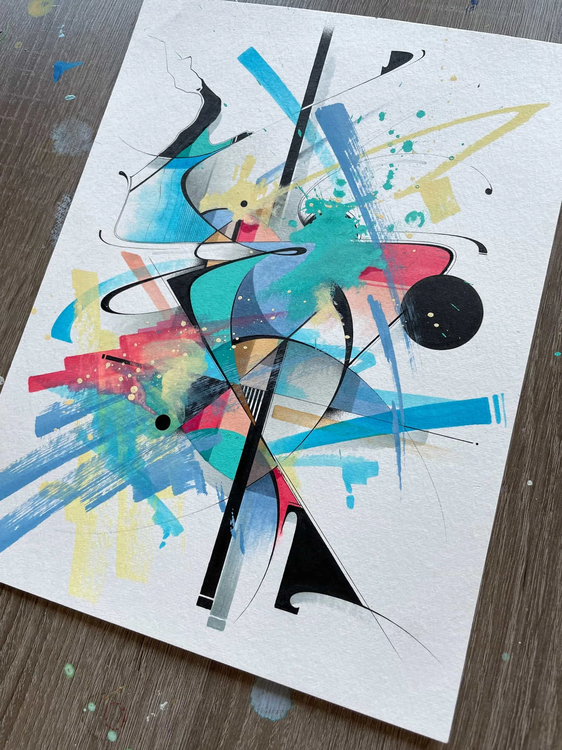 A colorful abstract painting on textured paper with splashes of blue, yellow, pink, and black, featuring dynamic lines and shapes.