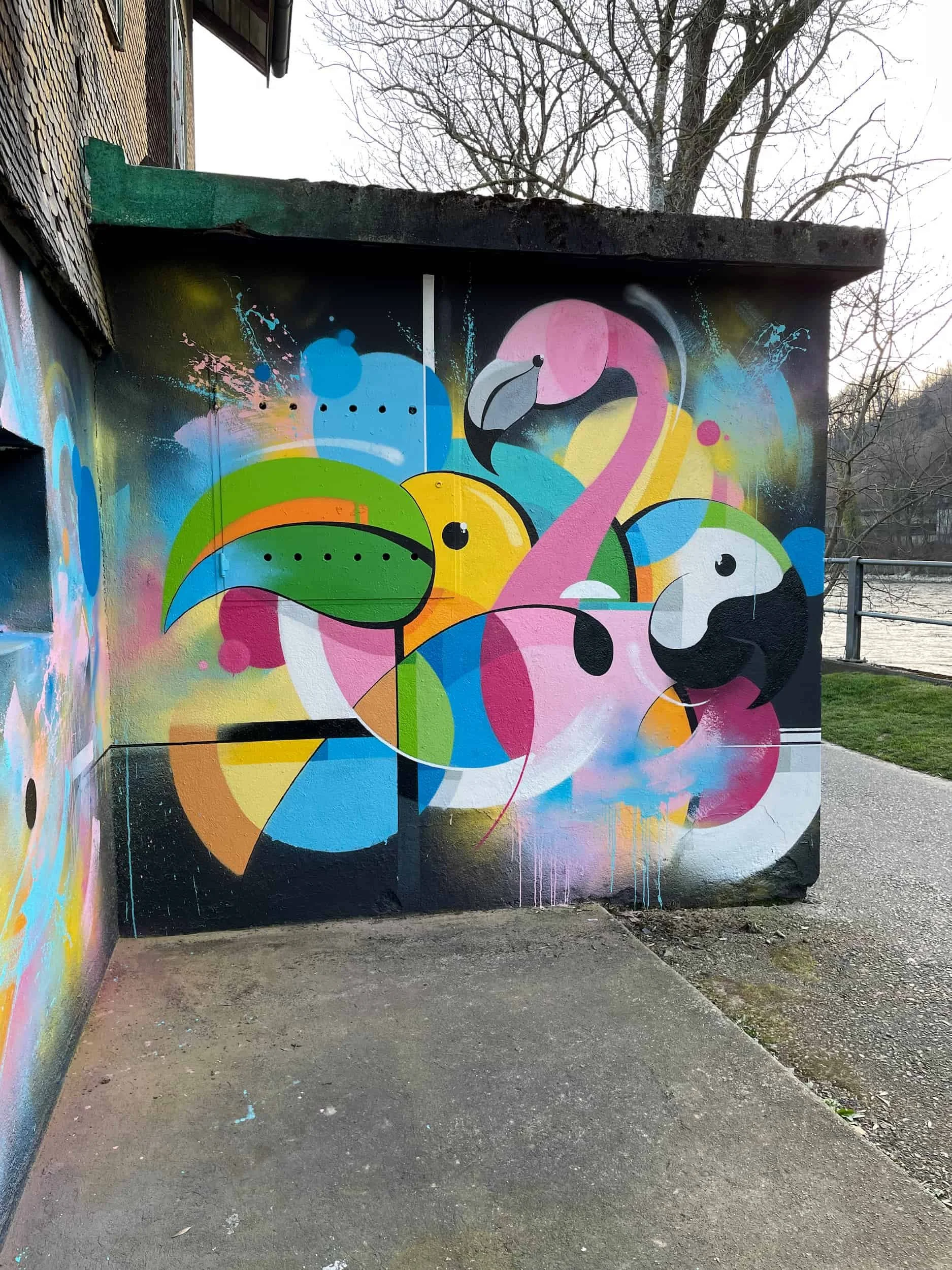 Colorful graffiti mural of stylized flamingos with pink, yellow, green, blue, black, and white hues on a building wall outdoors.