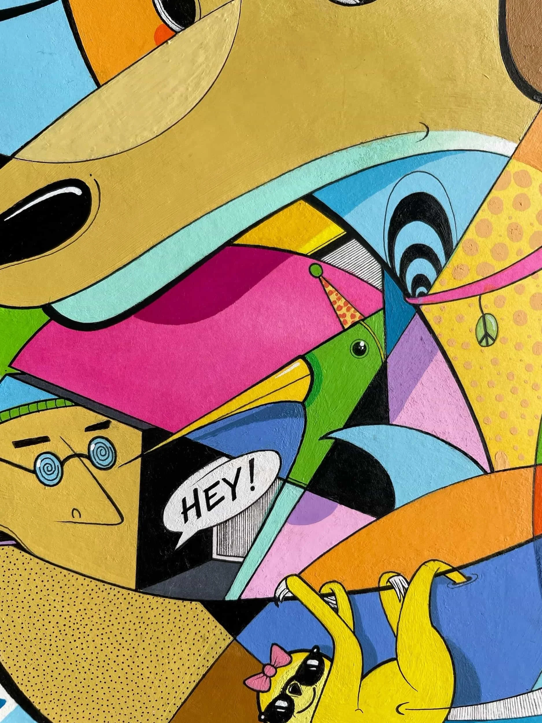 Close-up of a colorful, abstract cartoon mural with various characters, including a dog with big eyes and a pink bow, a yellow face with glasses and spiral eyes, and a pink speech bubble with the word 'HEY!'