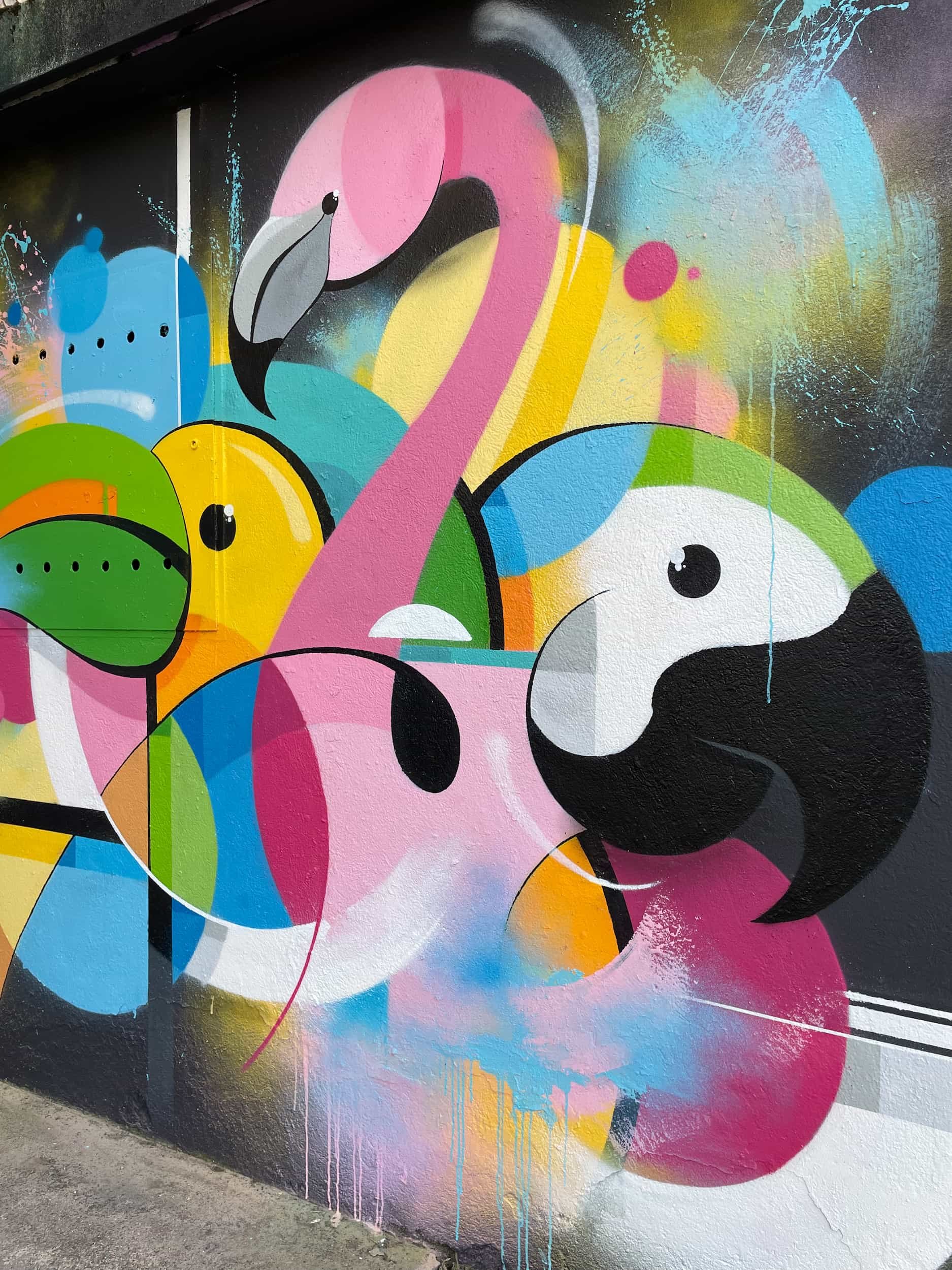 Colorful street art mural featuring abstract shapes, a pink flamingo, and stylized dog faces in vibrant colors.