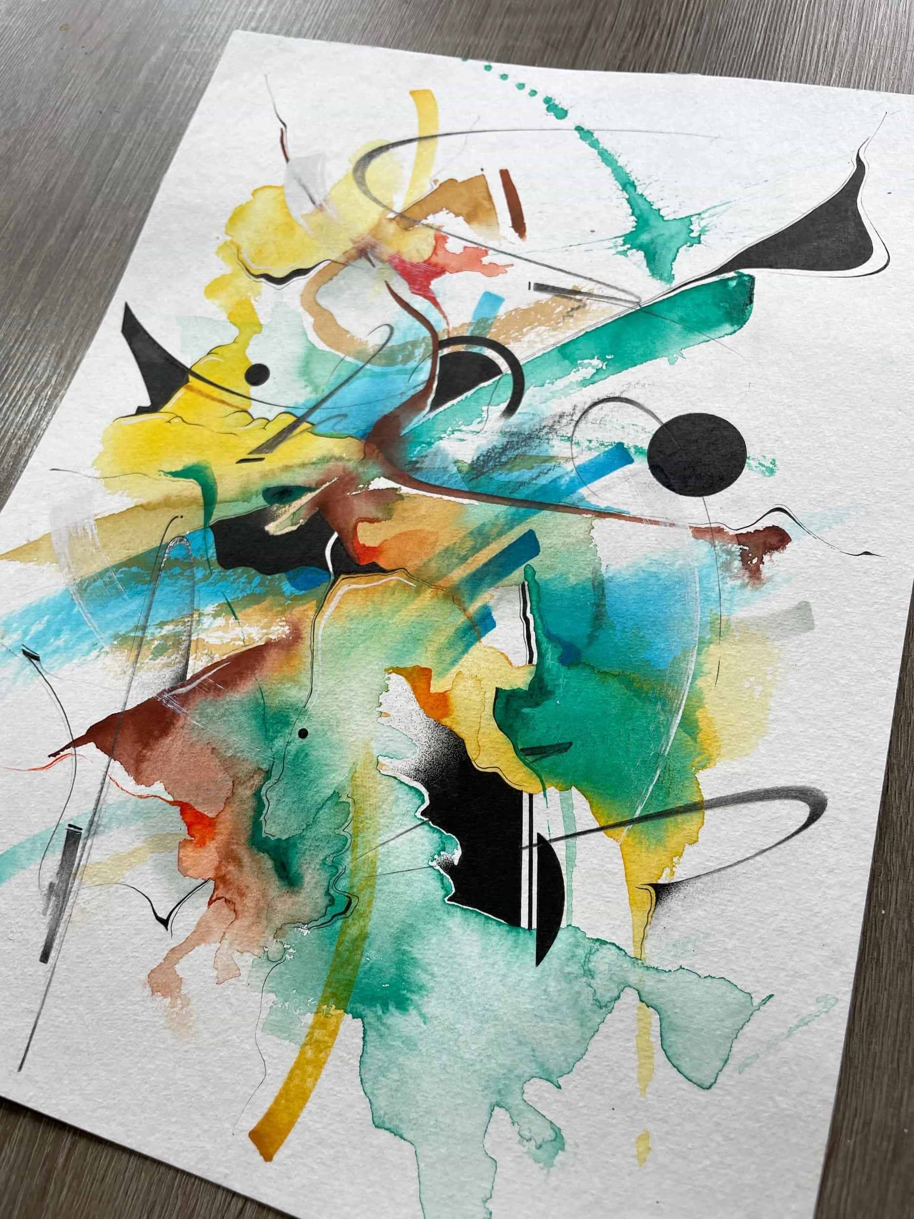 Abstract watercolor painting with splashes of yellow, blue, green, black, and brown, featuring curved and linear black ink lines on textured white paper.