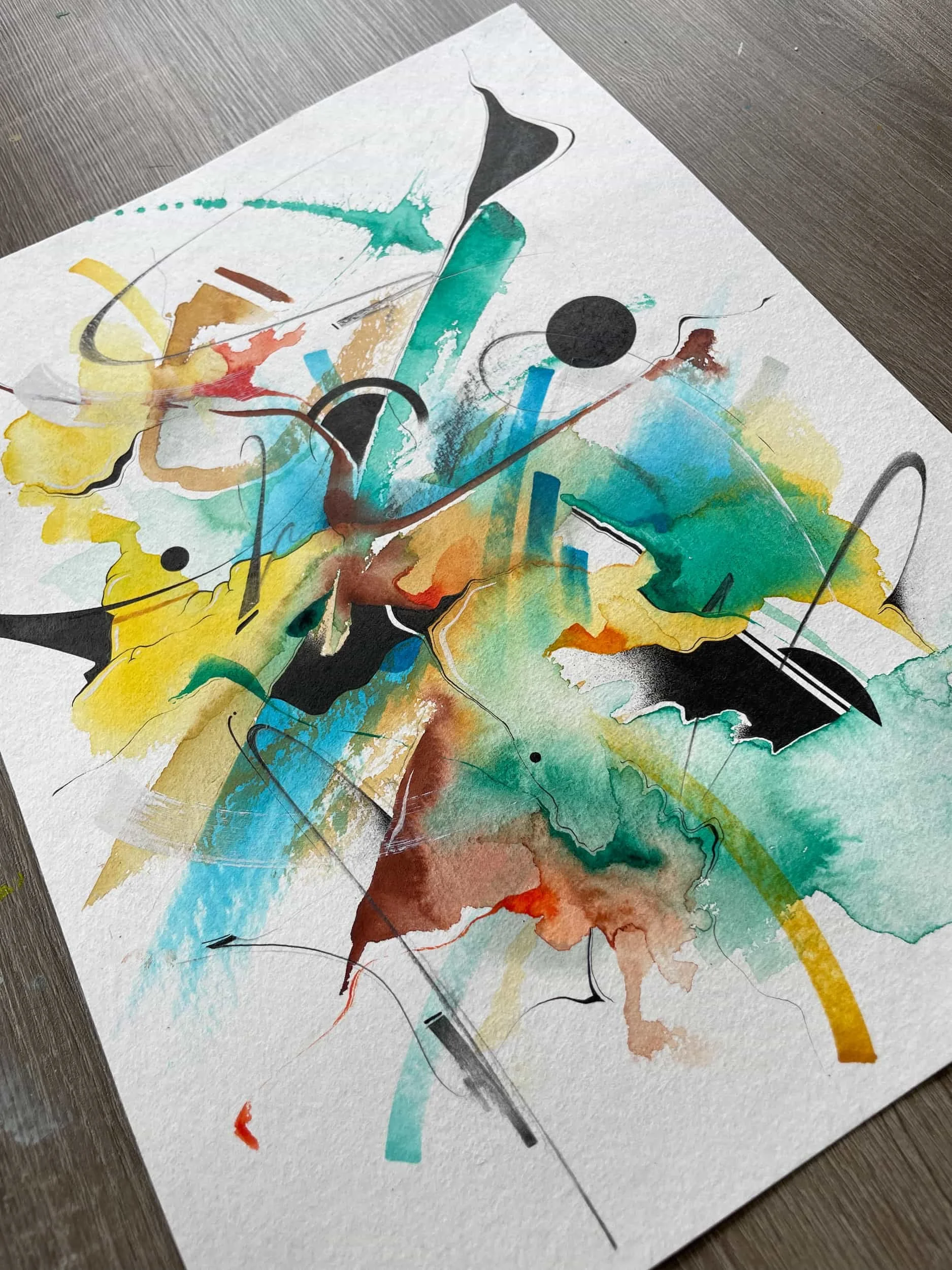 Abstract watercolor painting with splashes of yellow, blue, red, brown, black, and green on textured white paper.