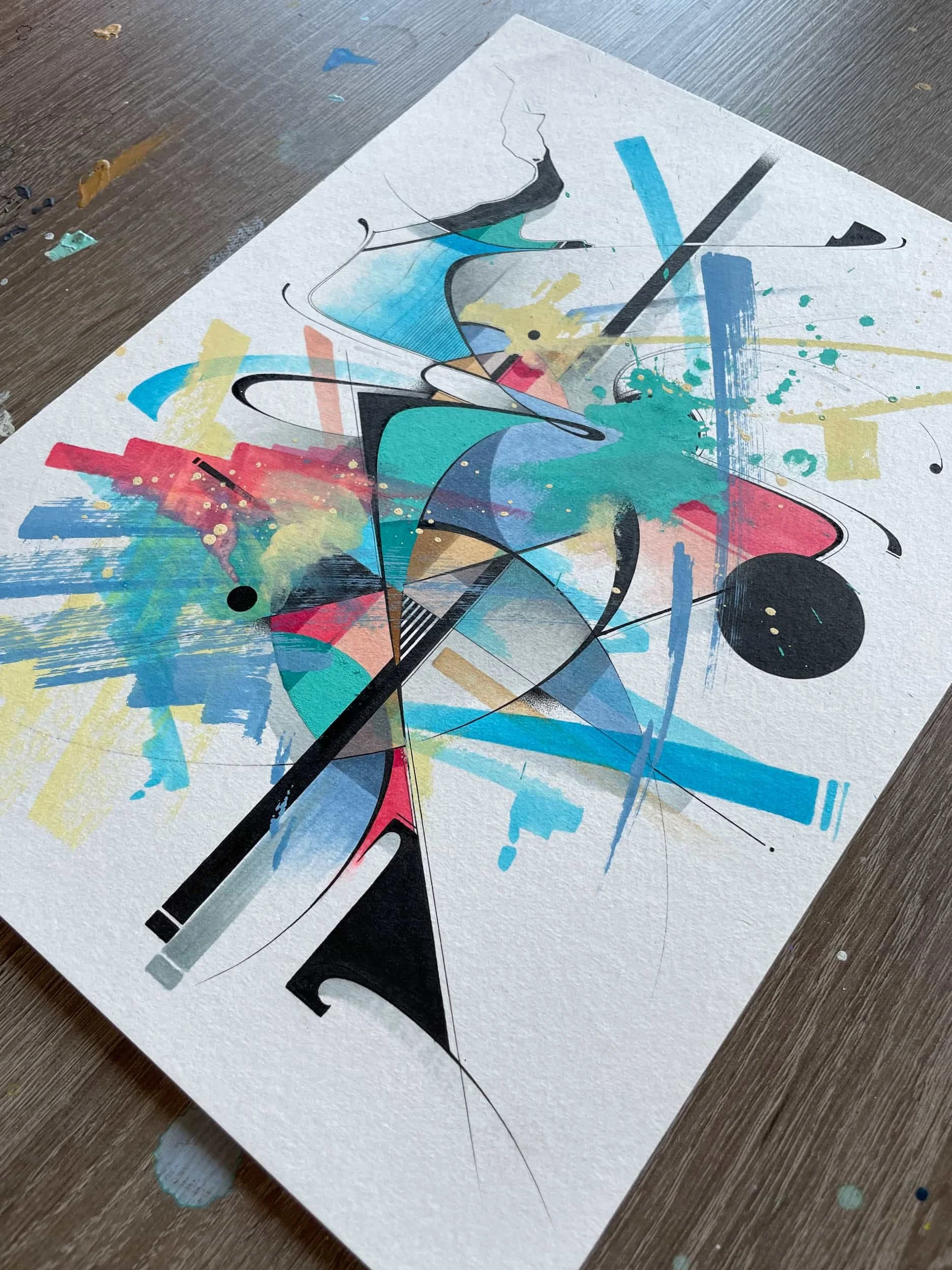 An abstract watercolor painting with splashes of blue, yellow, pink, and black, featuring geometric and curvilinear shapes on textured white paper.