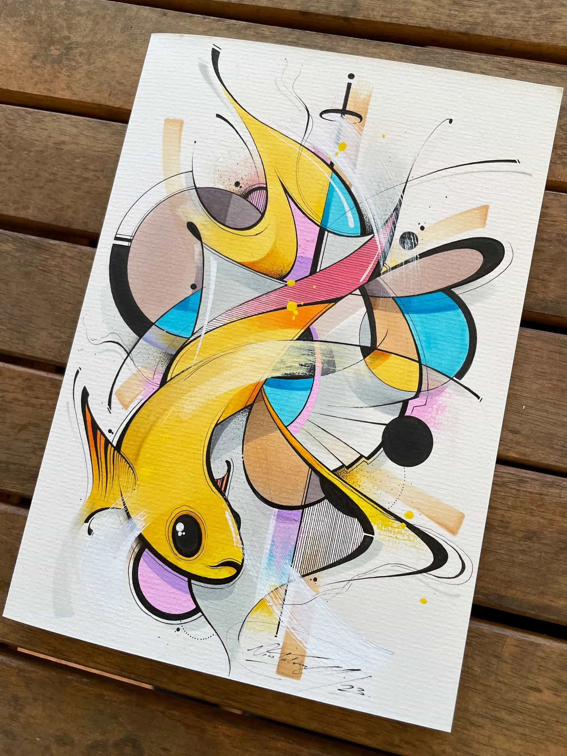 Colorful abstract artwork featuring a yellow fish with black eyes, surrounded by various shapes, lines, and splashes of color including blue, pink, black, and orange, on textured white paper.