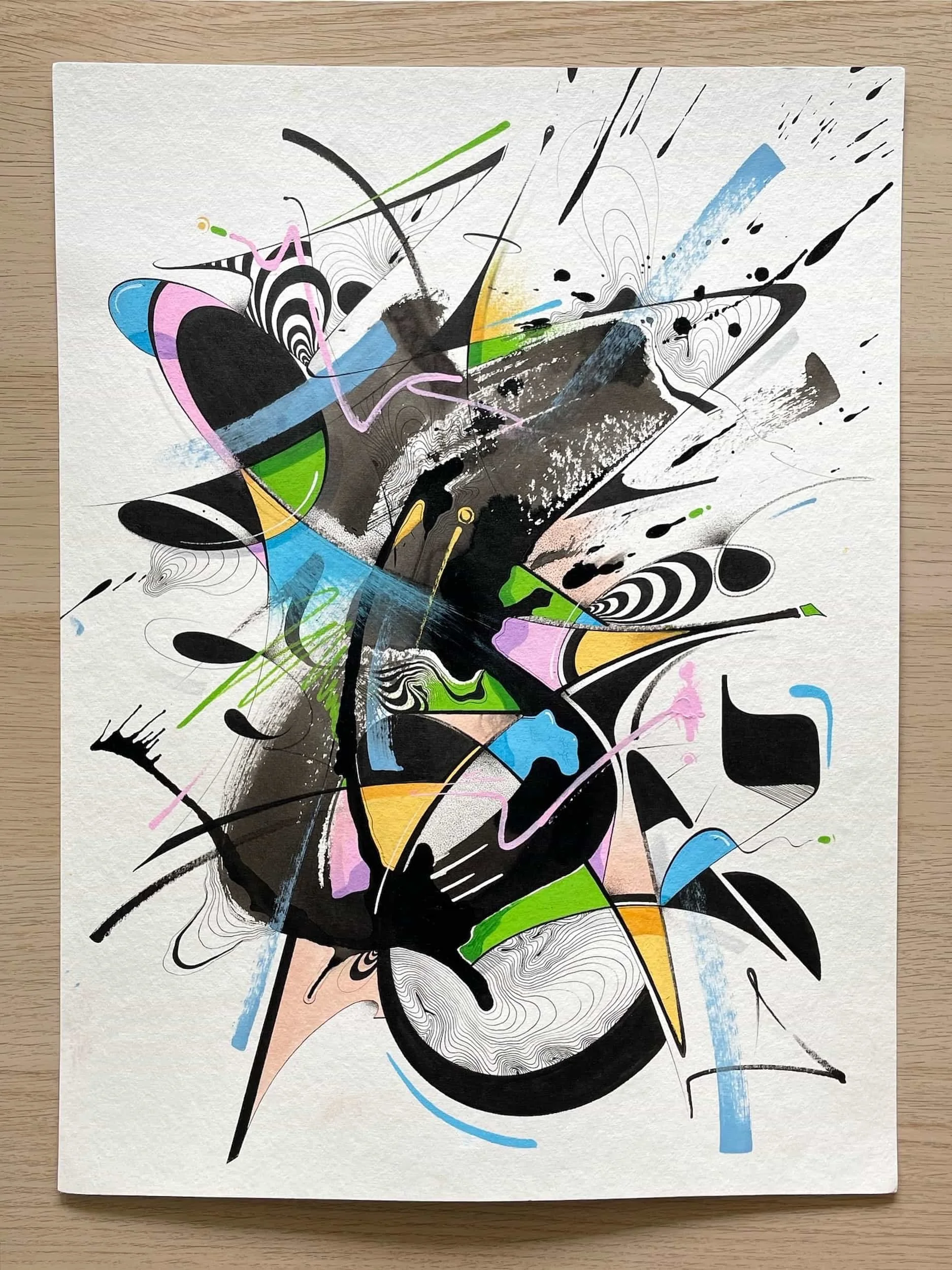 Abstract colorful painting with black, pink, green, yellow, blue, and white shapes and lines on a canvas placed on a wooden surface.