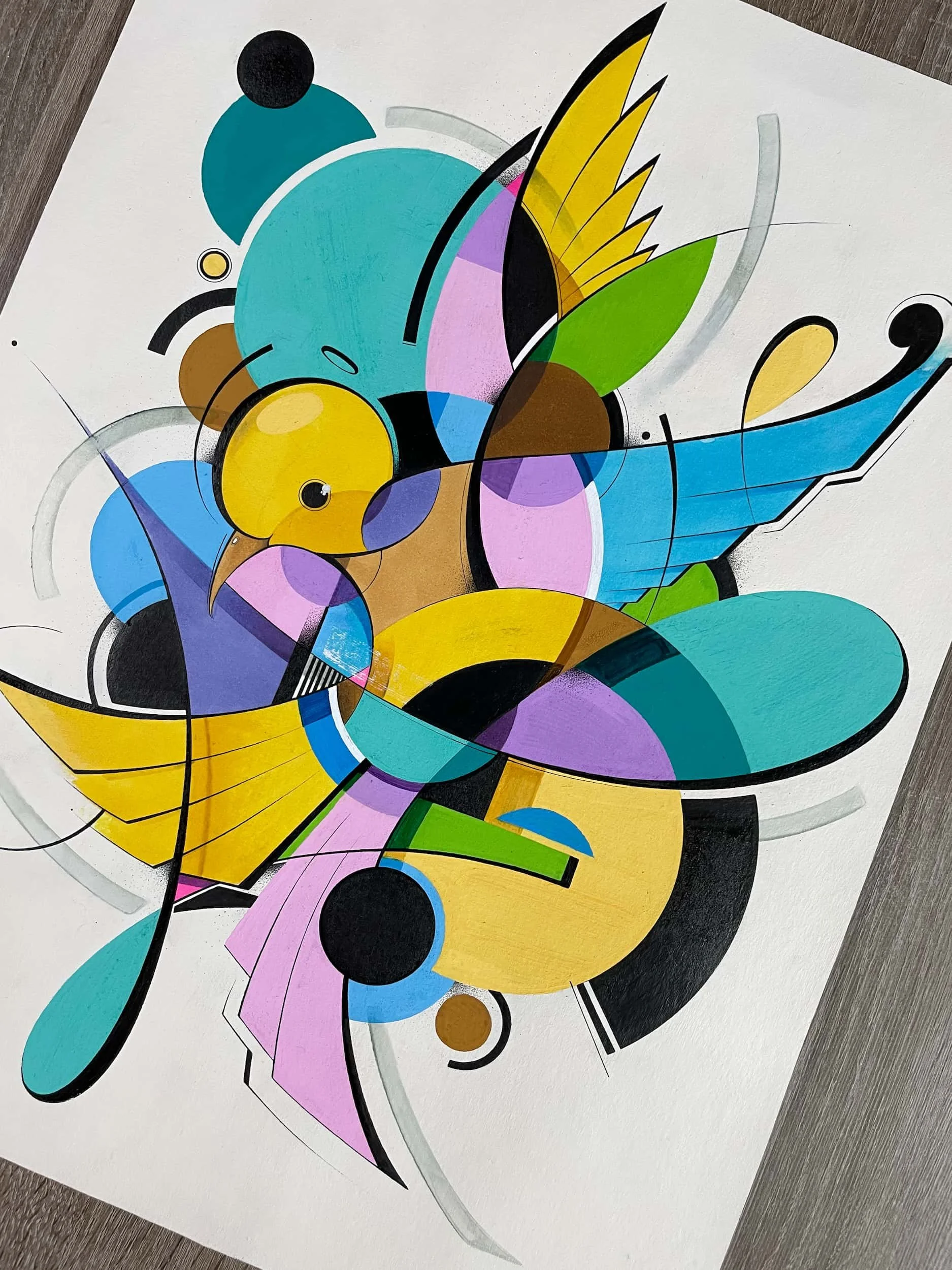 Abstract colorful drawing of a bird with shades of blue, yellow, purple, green, and black on white paper placed on a wooden surface.