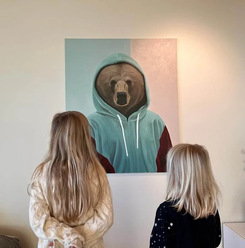 To barn som ser på et maleri av en bjørn som har på seg en grønn hette og jakke.