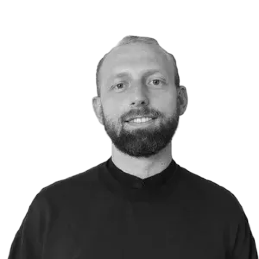 Portrait eines Mannes mit Bart und kurzer Frisur, trägt einen schwarzen Pullover, steht vor einem schwarzen Hintergrund.