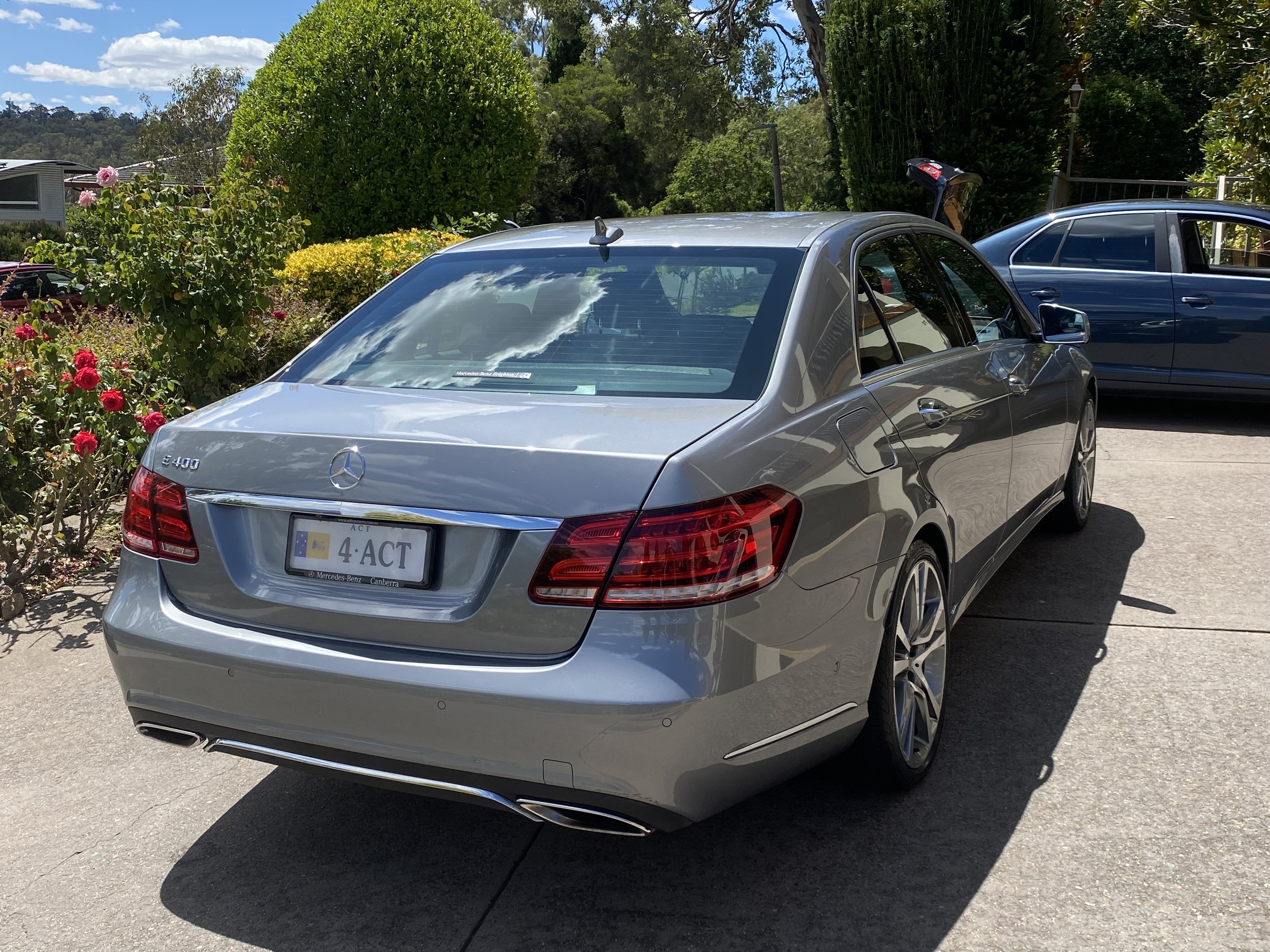 Silver Mercedes-Benz E-Class E400 parked on driveway with bushes and trees in background.