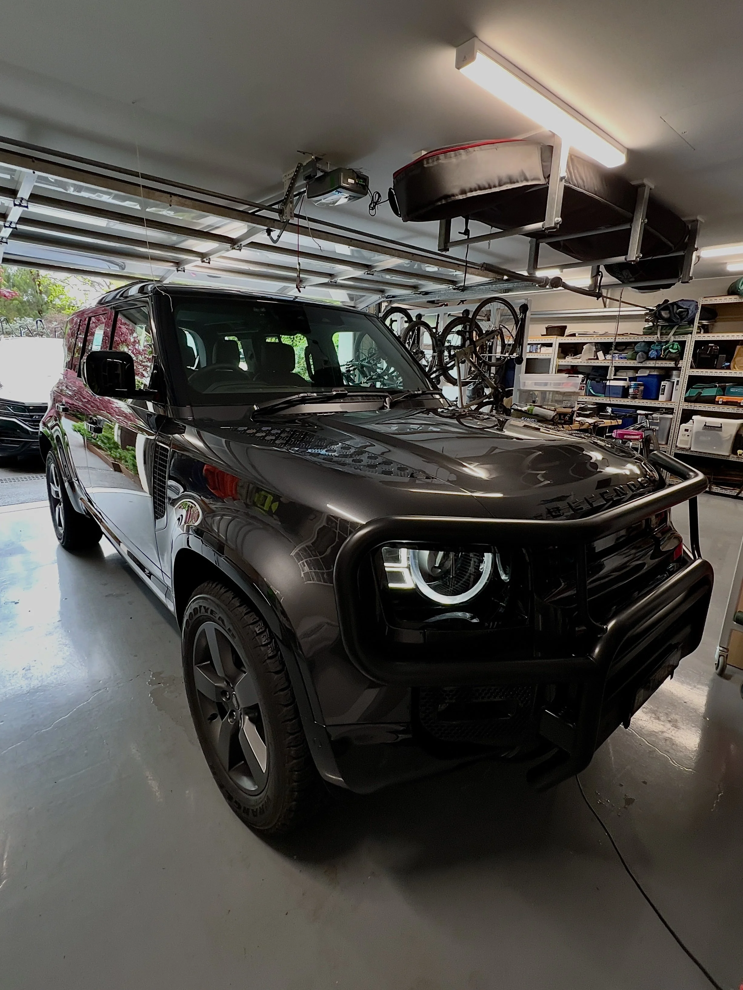 Black SUV with a bull bar in a garage with shelves and bikes in the background.