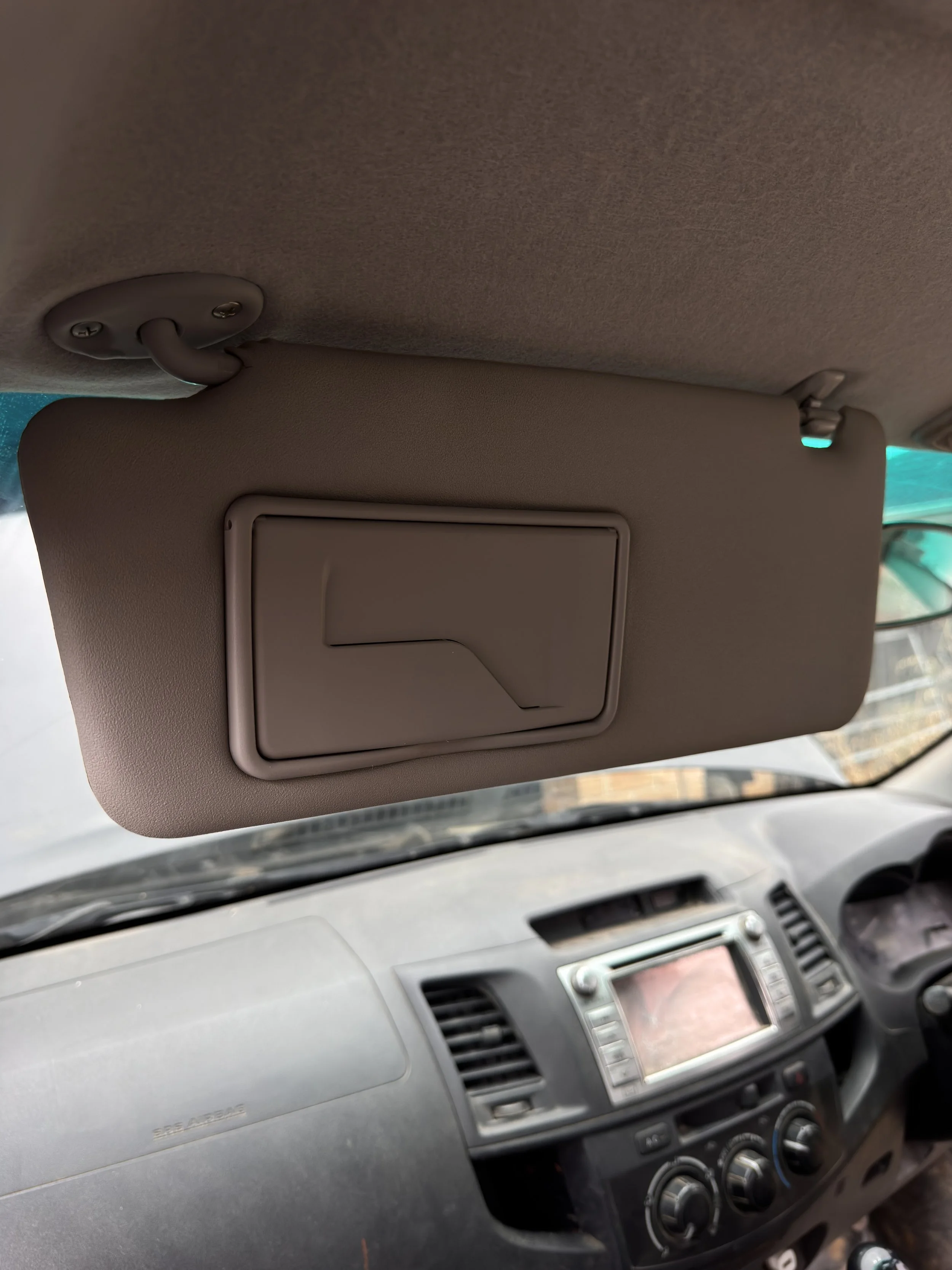 View of the interior of a vehicle showing the driver's dashboard and a sun visor with a mirror cover in the up position.