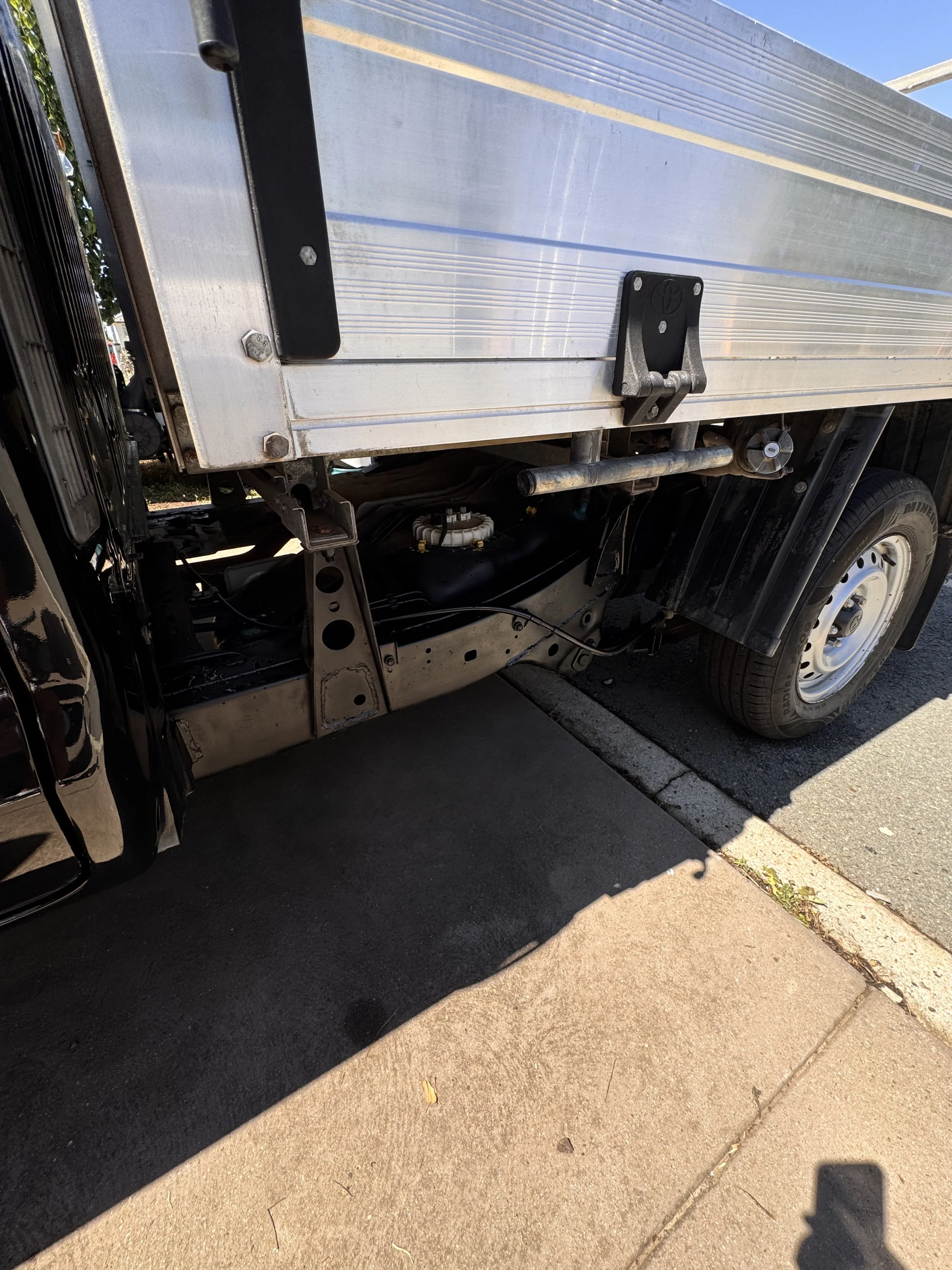 Close-up of the side of a flatbed truck, showing the wheel, metal frame, and part of the cargo area with aluminum siding.