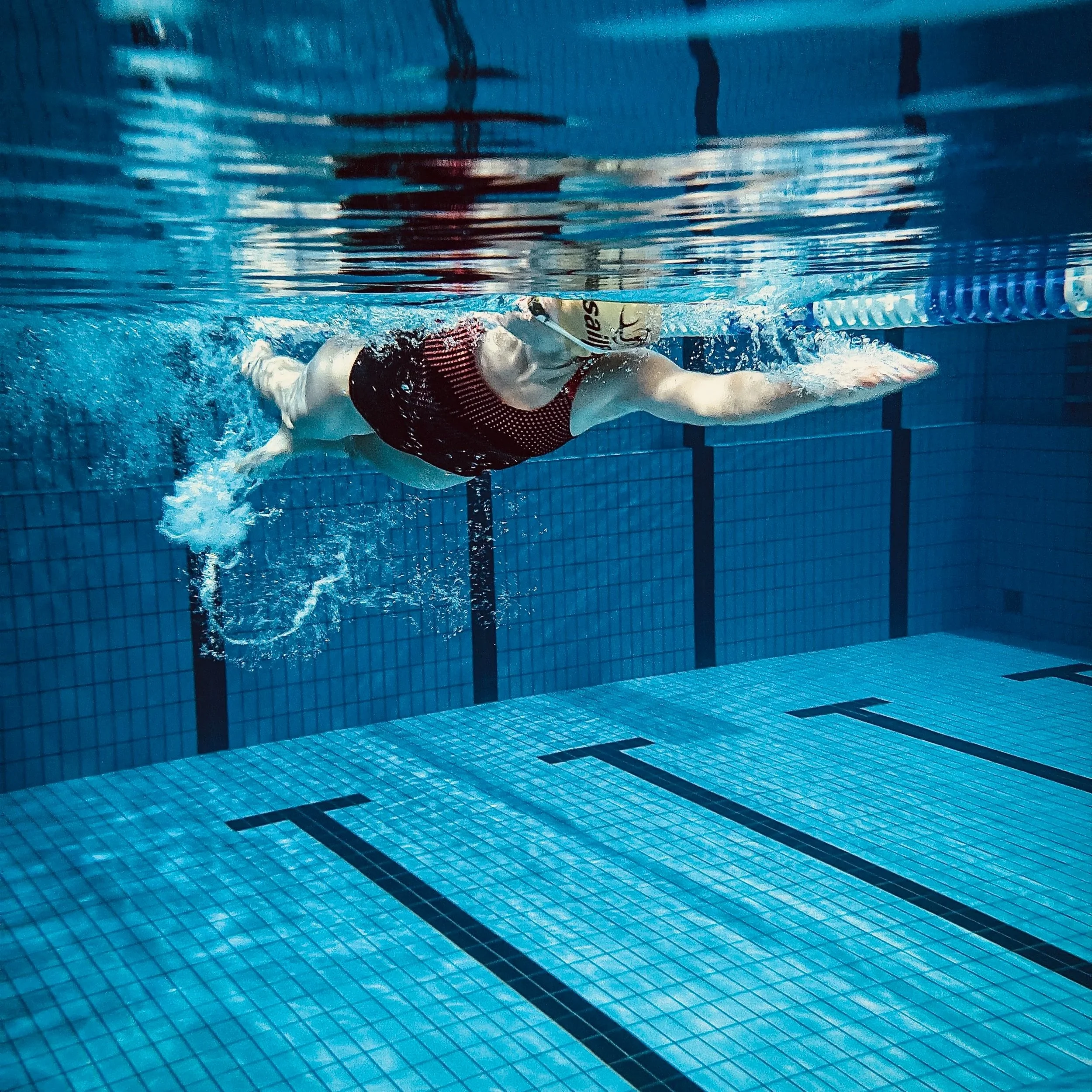 Eine Person schwimmt im Schwimmbad, trägt eine rote Schwimmbekleidung und verwendet eine schwarze Schwimmbrille.
