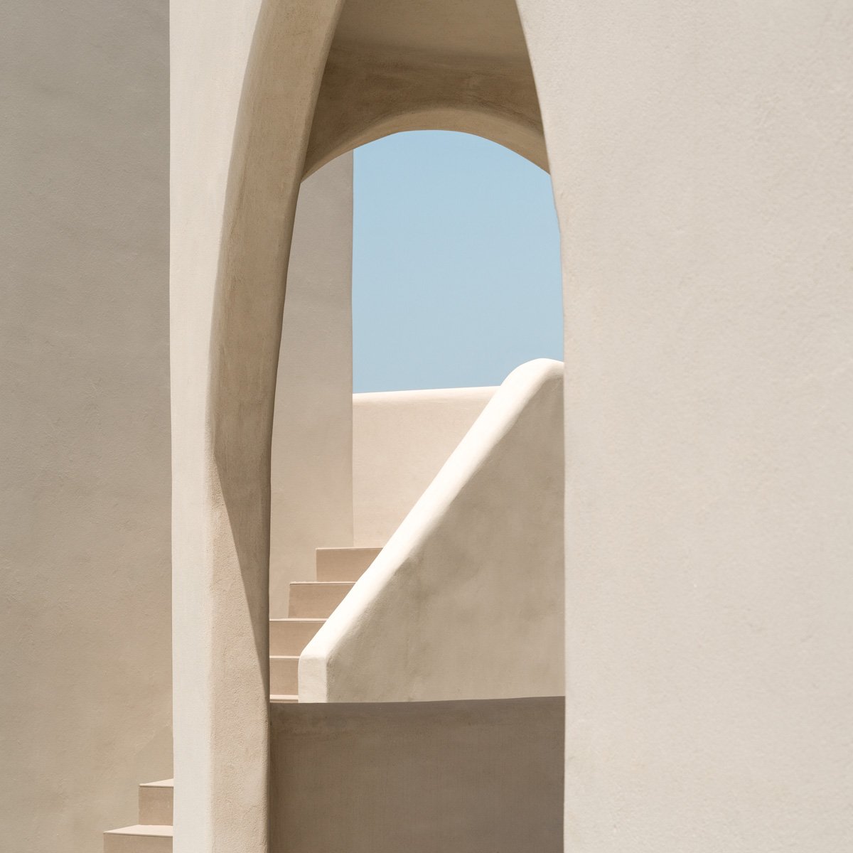 Minimalist beige architectural scene with stairs and rounded openings, bright blue sky in the background.