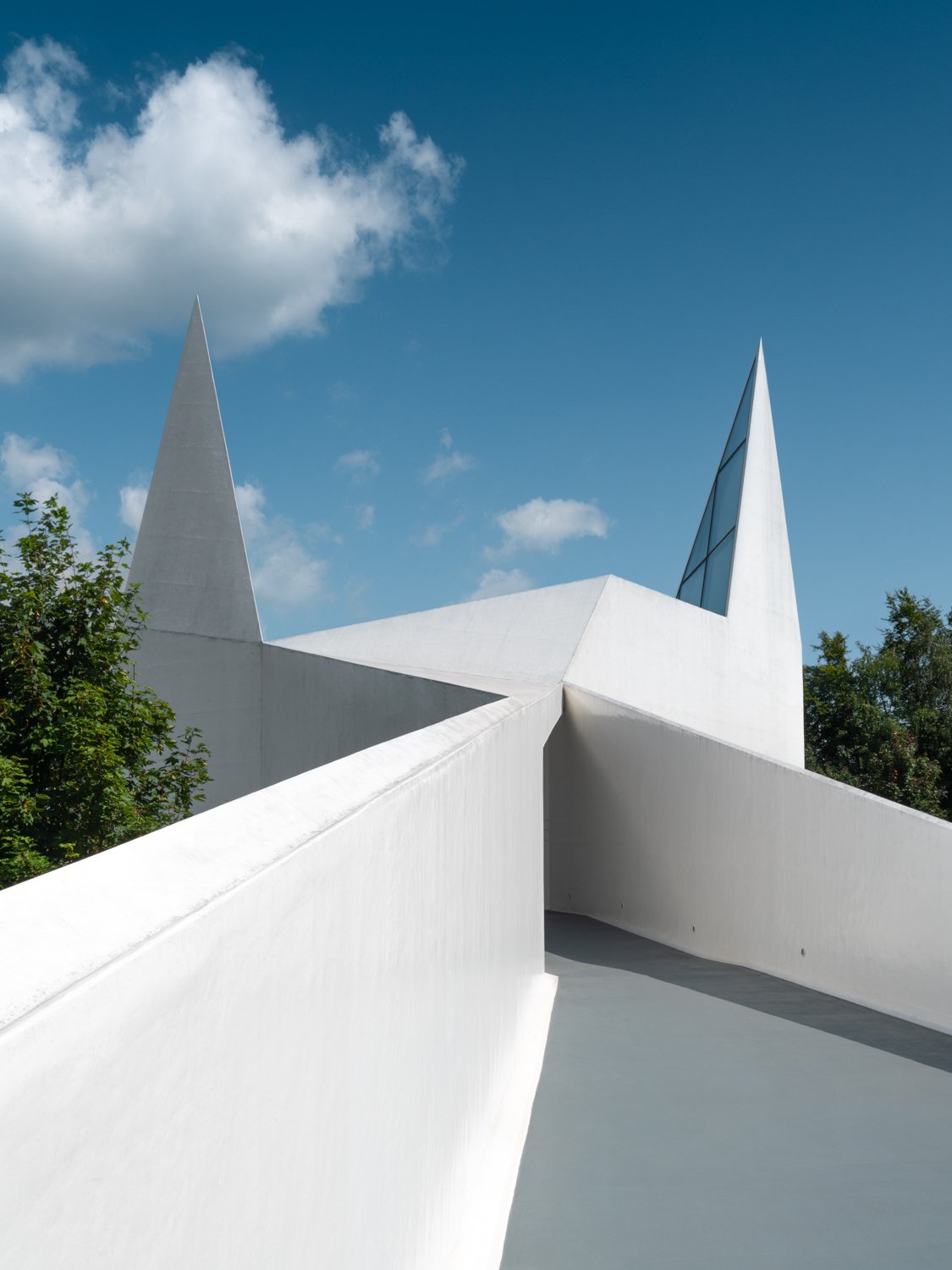 Modern architectural building with white angular surfaces and sharp peaks against a blue sky with clouds