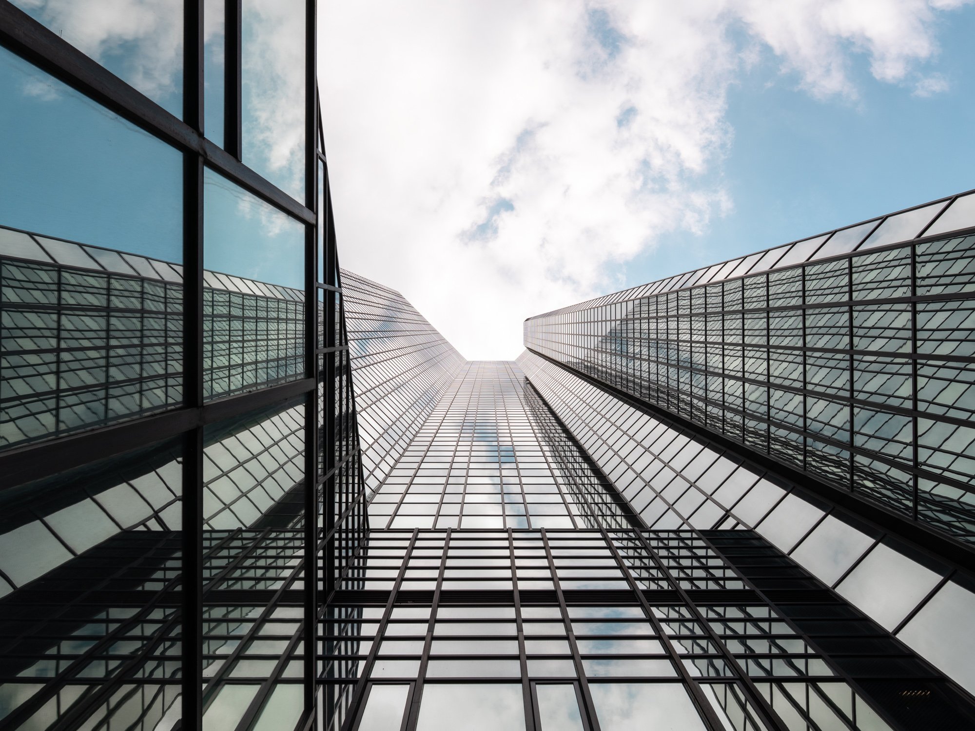 Looking up at tall modern glass skyscrapers reflecting the sky and clouds.