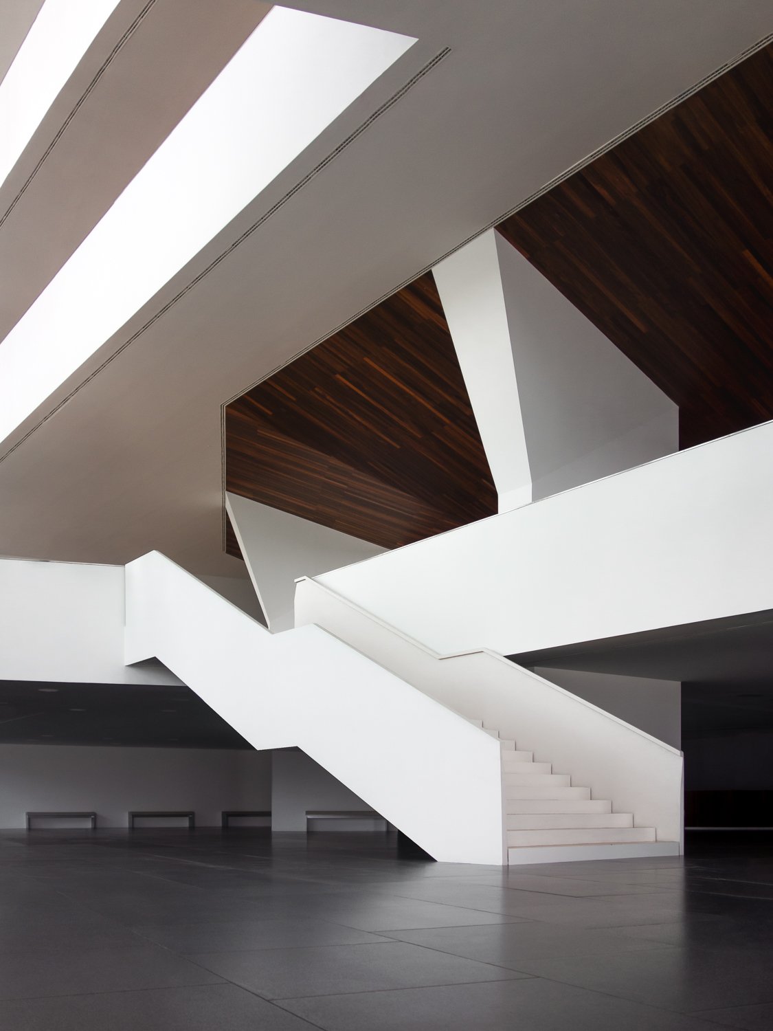 Modern interior with a white staircase, dark tile flooring, and wooden ceiling panels.