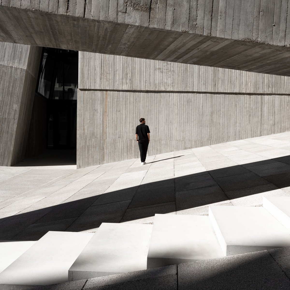 A person walking along a concrete structure with modern, angular architecture and stark shadows.