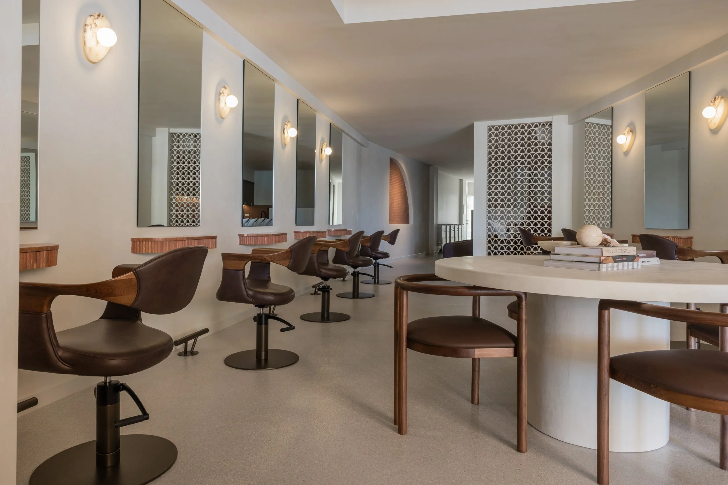 Interior of a modern hair salon or beauty studio with styling chairs and framed mirrors along the wall, dim lighting, and a neutral color palette.