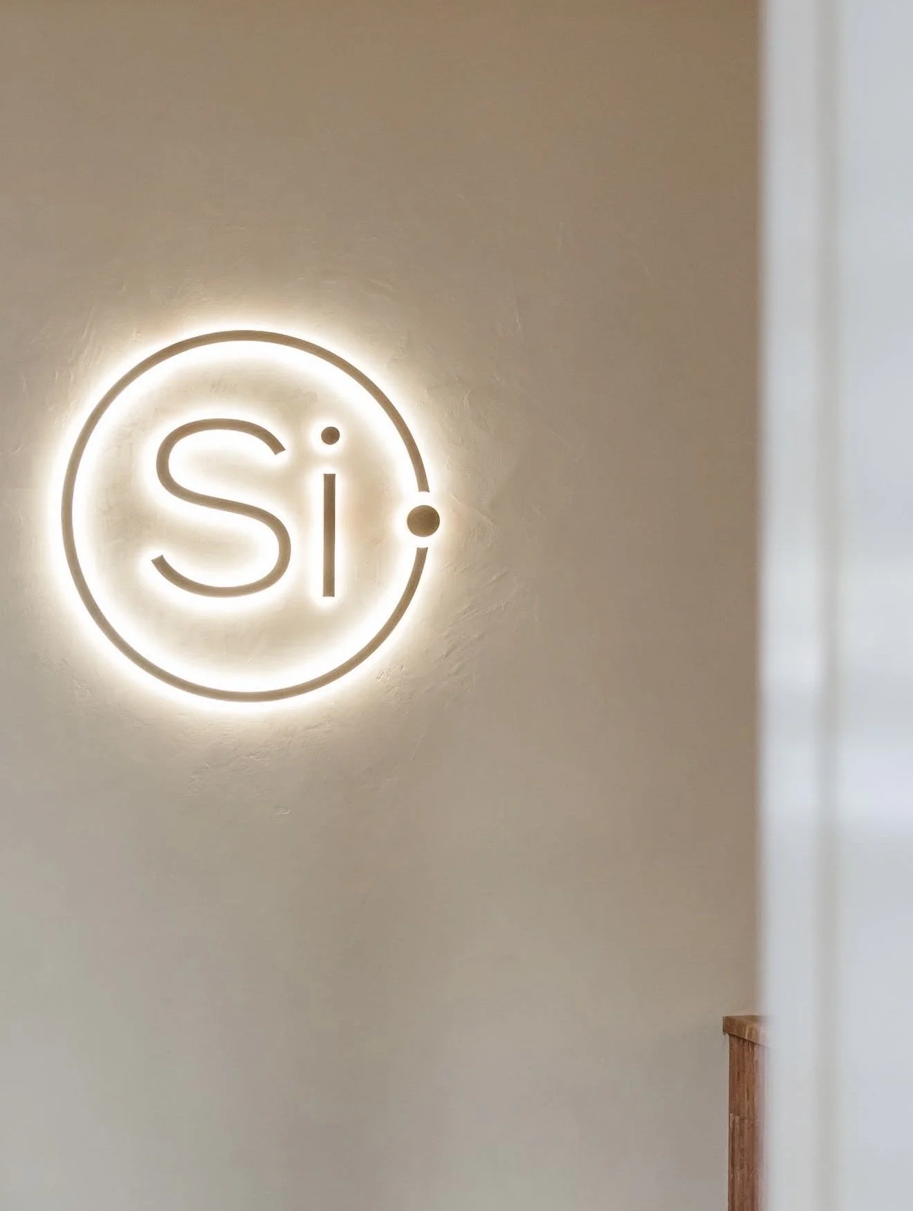 A wall with illuminated sign saying 'Si' inside a circle, with a dot near the circle.