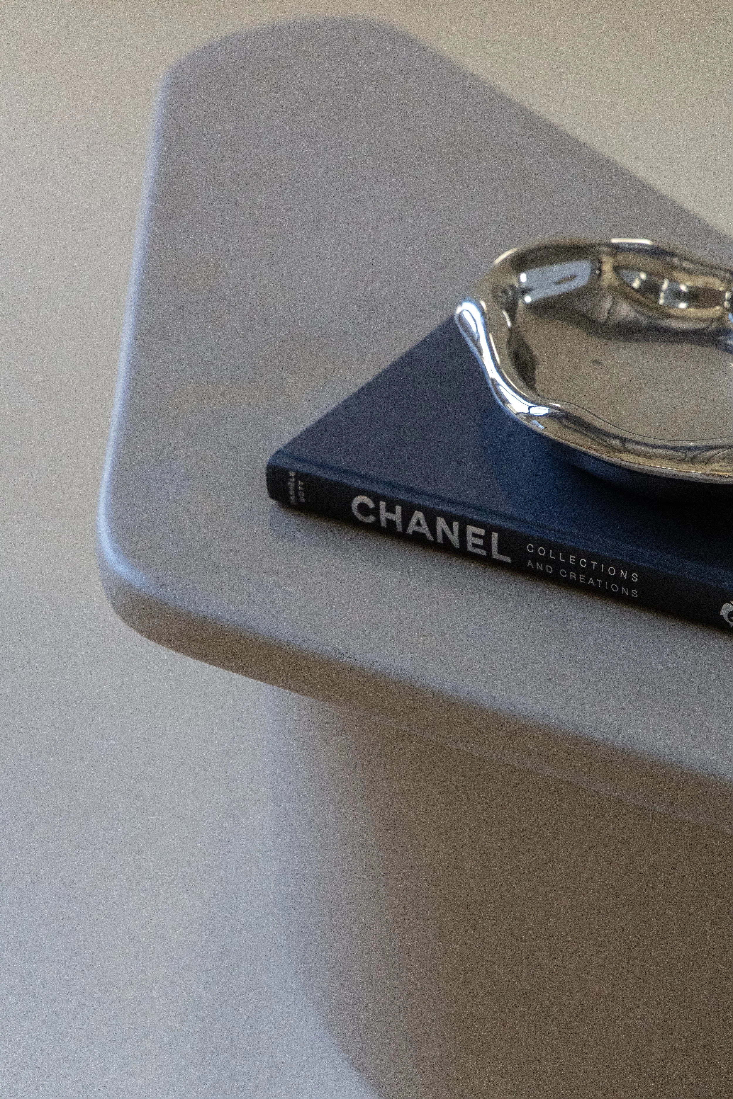 A silver dish on top of a navy blue Chanel book placed on a light-colored table.