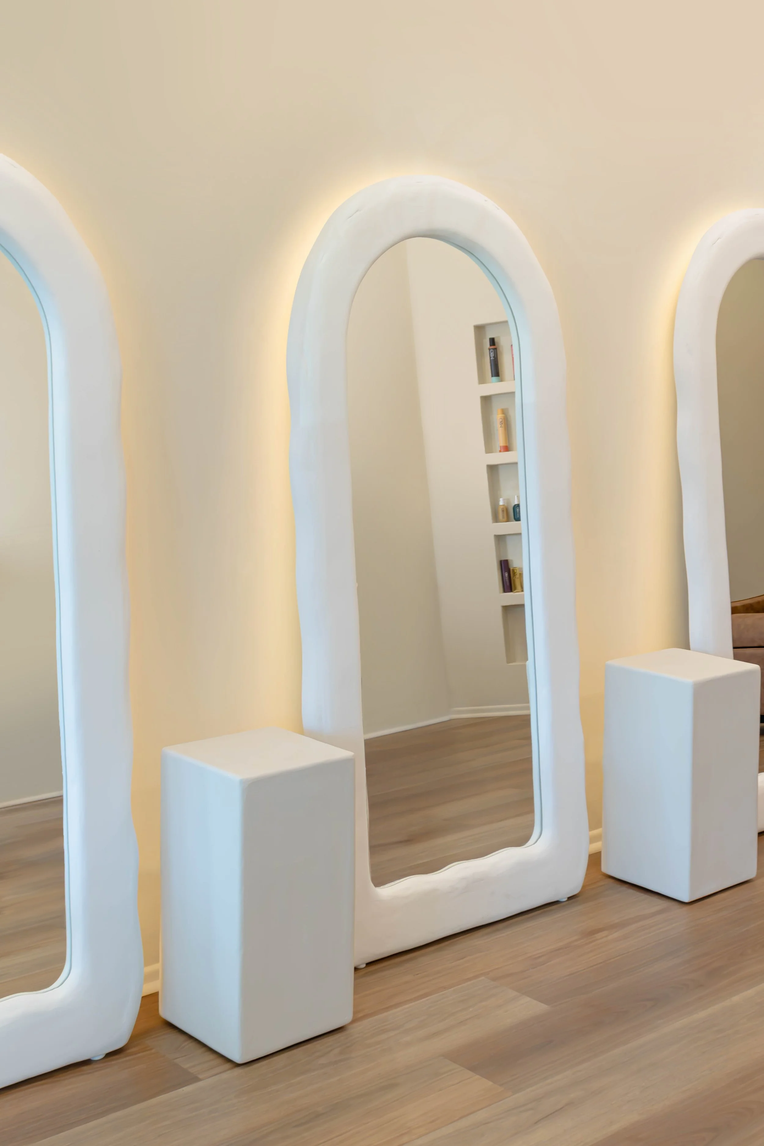 Modern interior with curved white archways, small display shelves, and seating areas, featuring warm lighting and wood flooring.