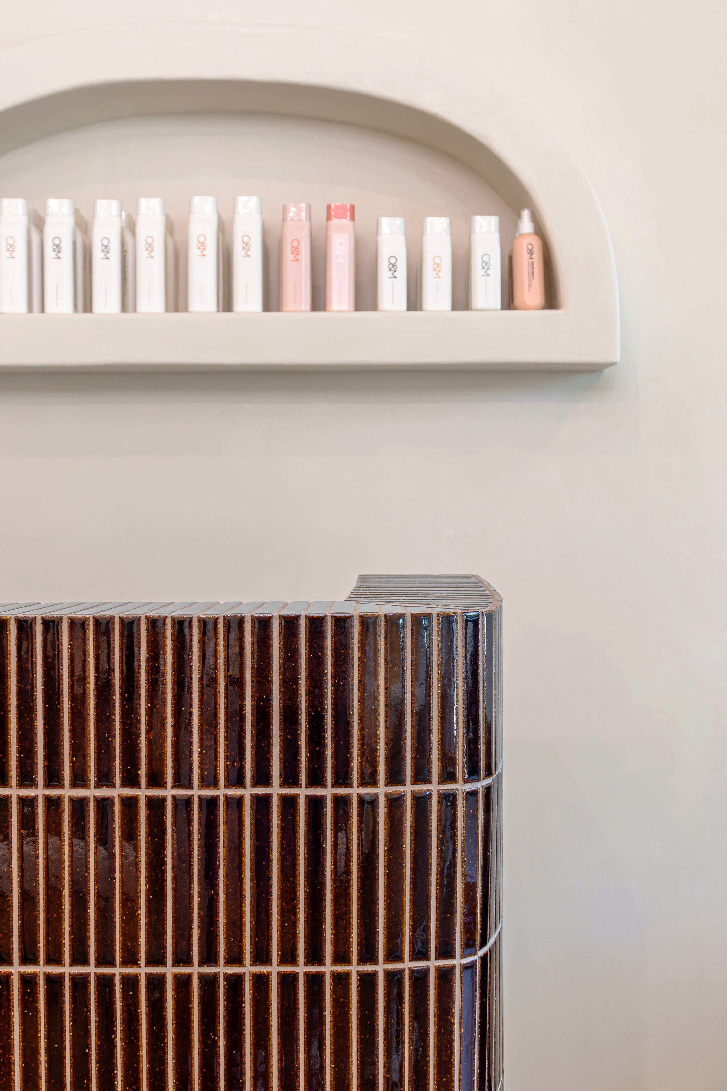 Shelves with skincare or cosmetic bottles and jars on a wall above a dark brown textured counter.