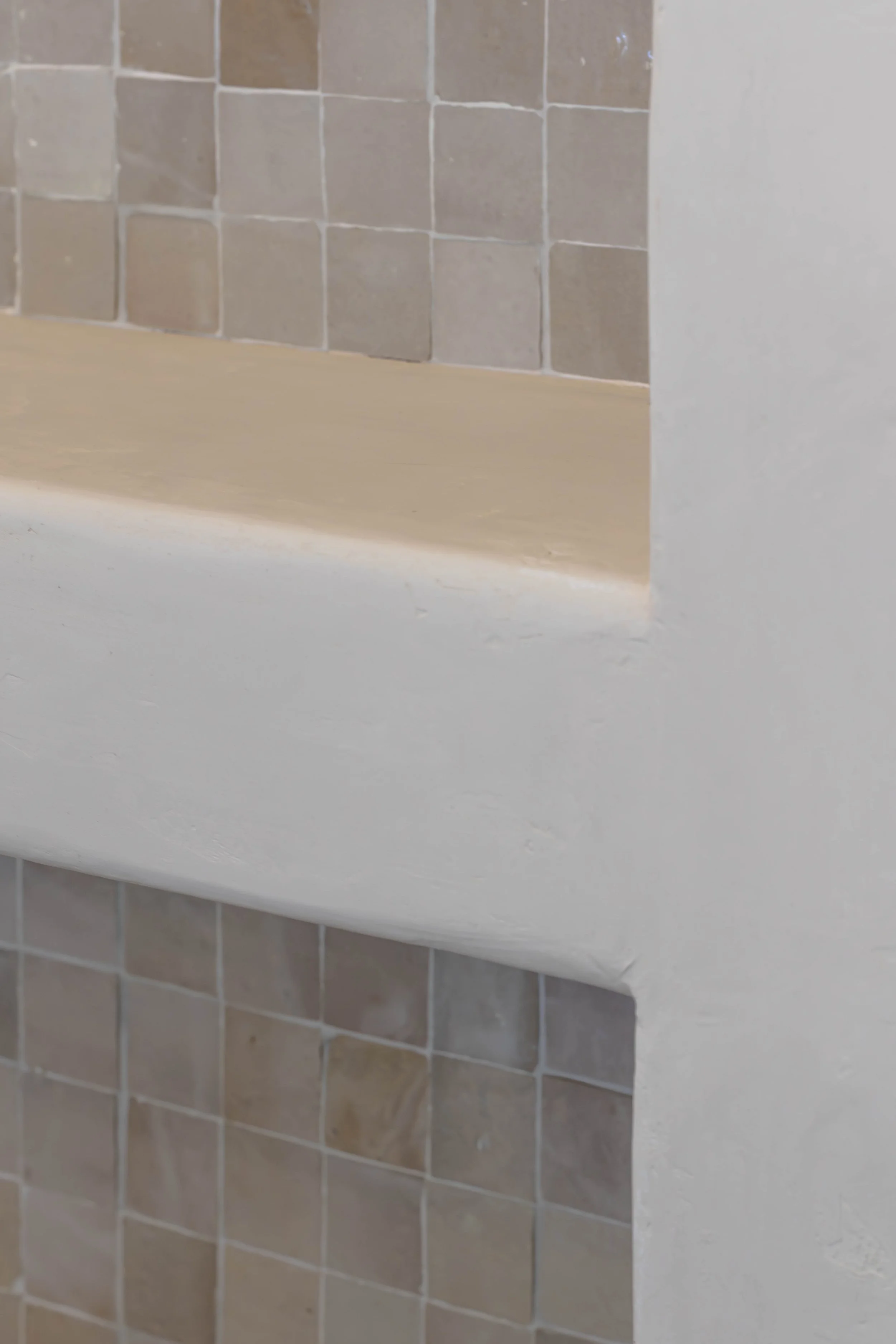Close-up of a shower wall with beige tiles and a white painted ledge or shelf.