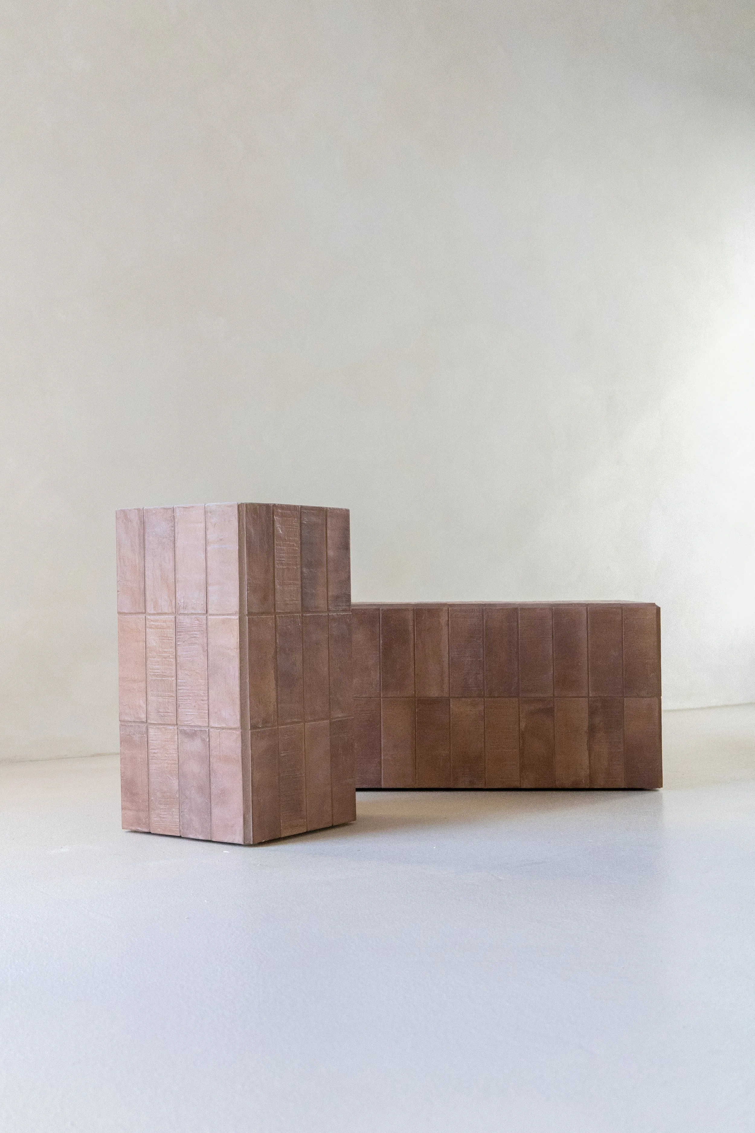 A minimalist wooden bench with a T-shaped design against a plain, neutral-colored wall.