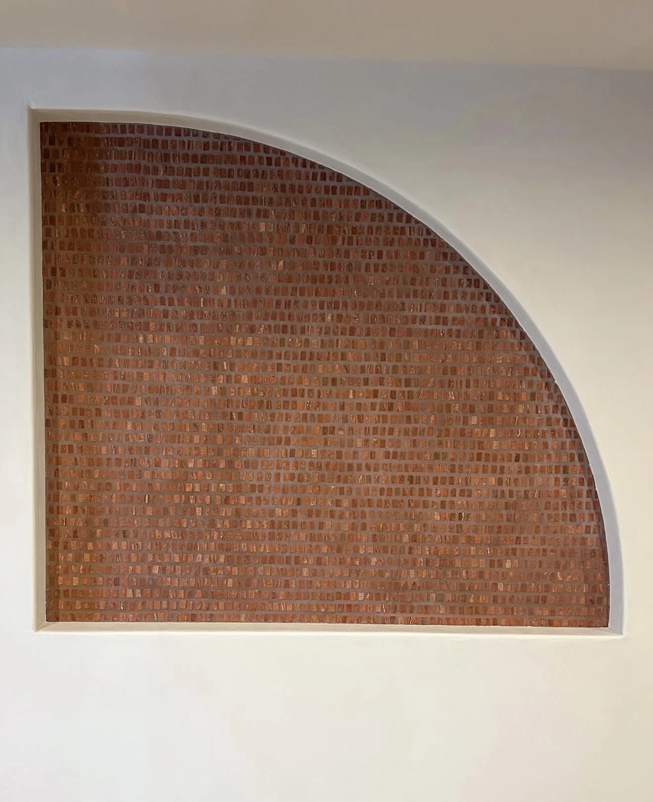 Close-up of a rectangular red mosaic tile wall in a white-frame alcove with a curved top.
