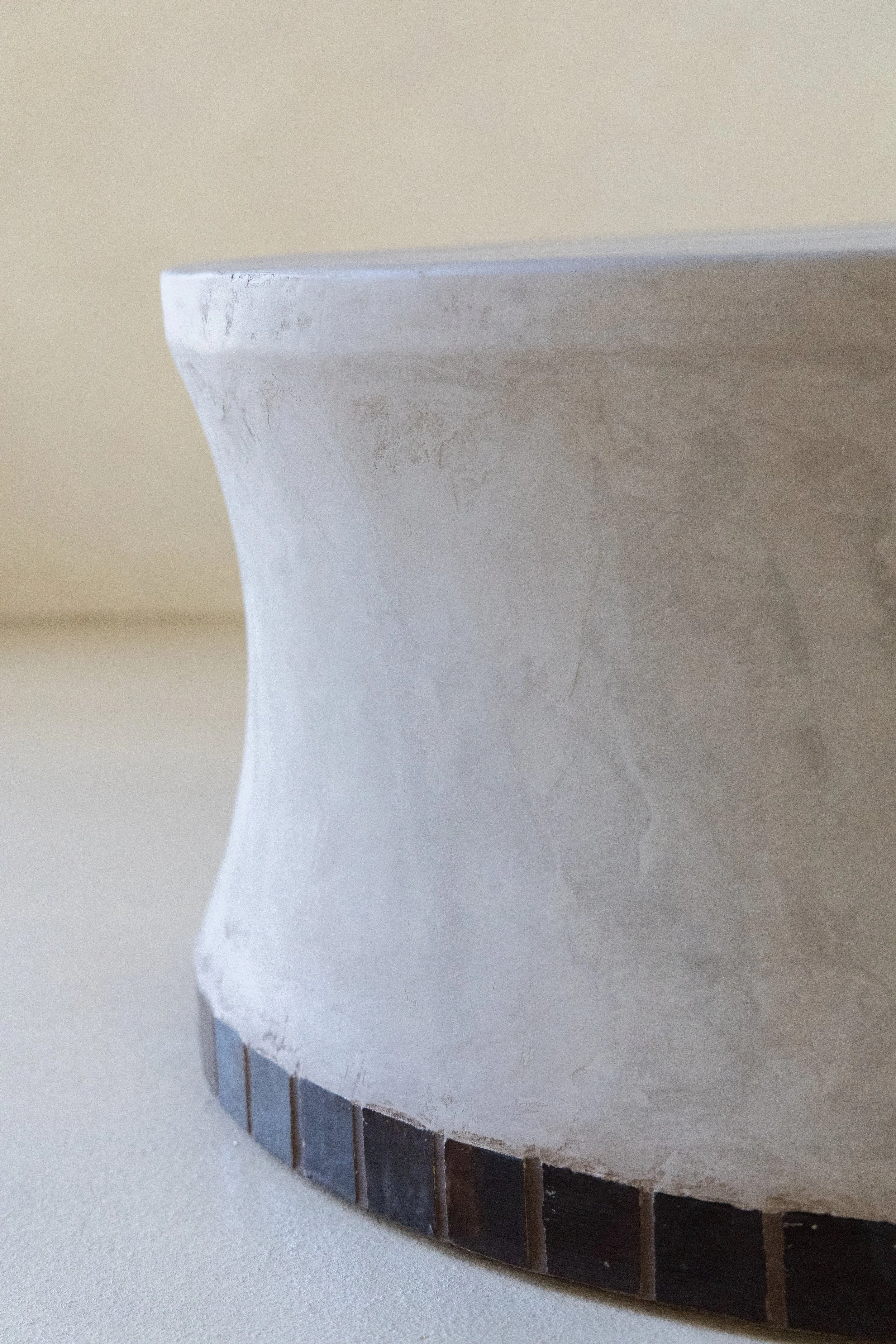 Close-up of a small stool or table with a curved, textured surface and a tiled bottom edge.