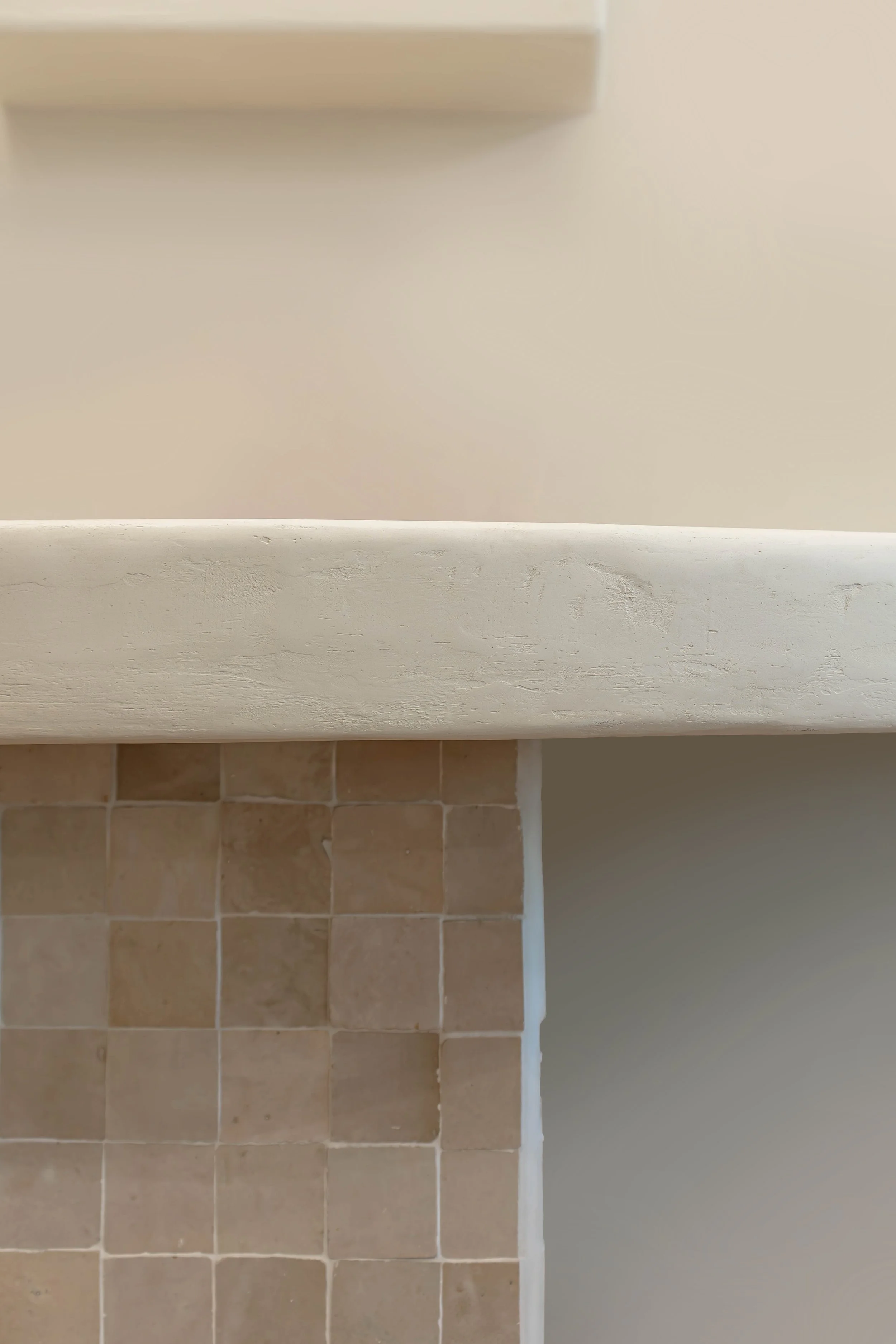 Close-up of a beige tiled wall with part of a white painted cabinet or counter above it, and a dark gray wall on the right side.