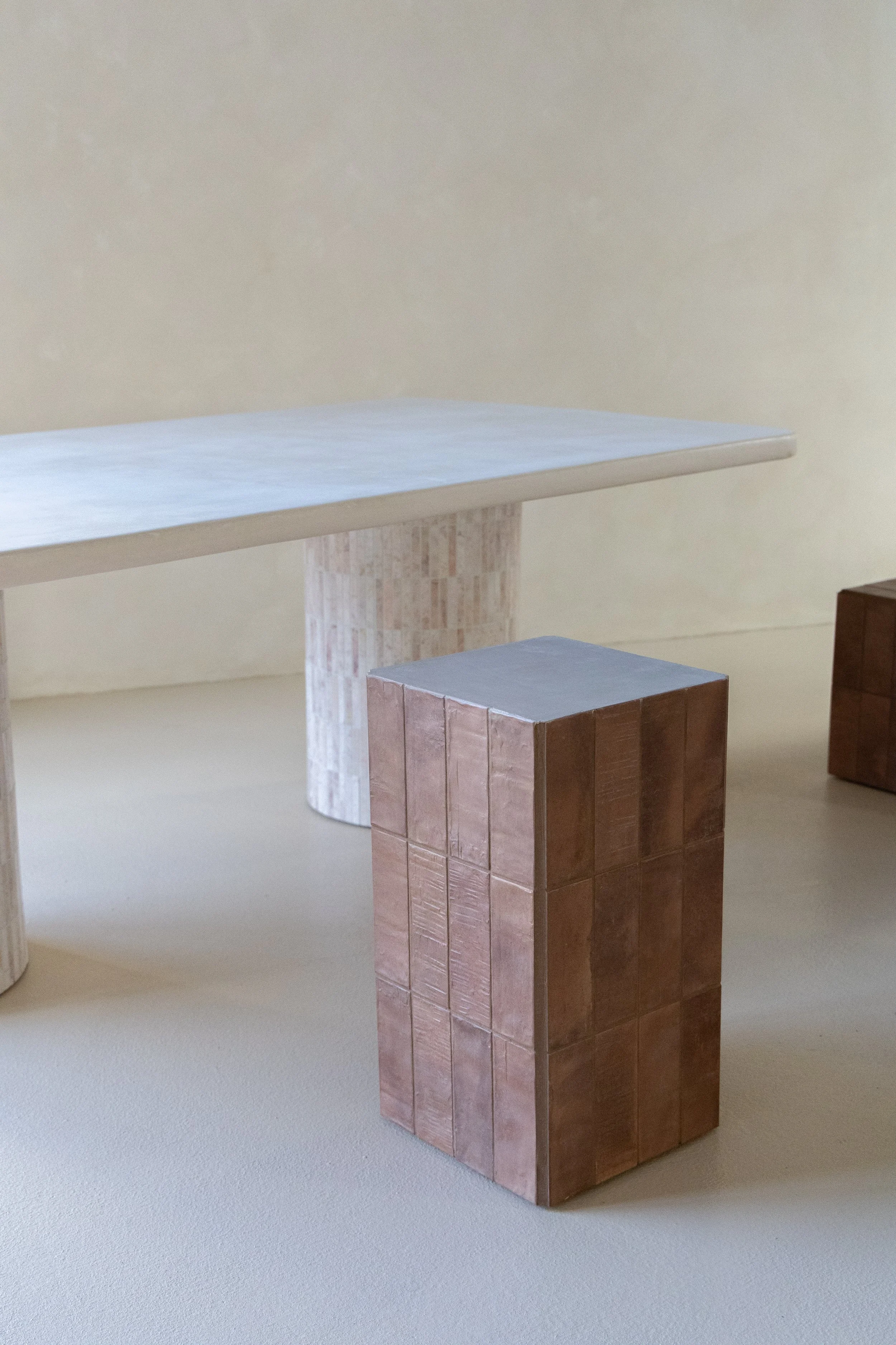 Minimalist wooden table with square brick-like supports, in a room with plain beige walls and carpeted floor.