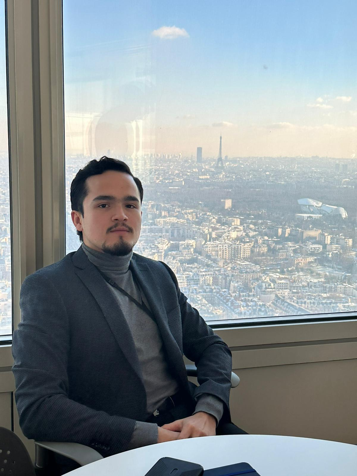 A man sitting at a table with a city view of Paris in the background, including the Eiffel Tower.
