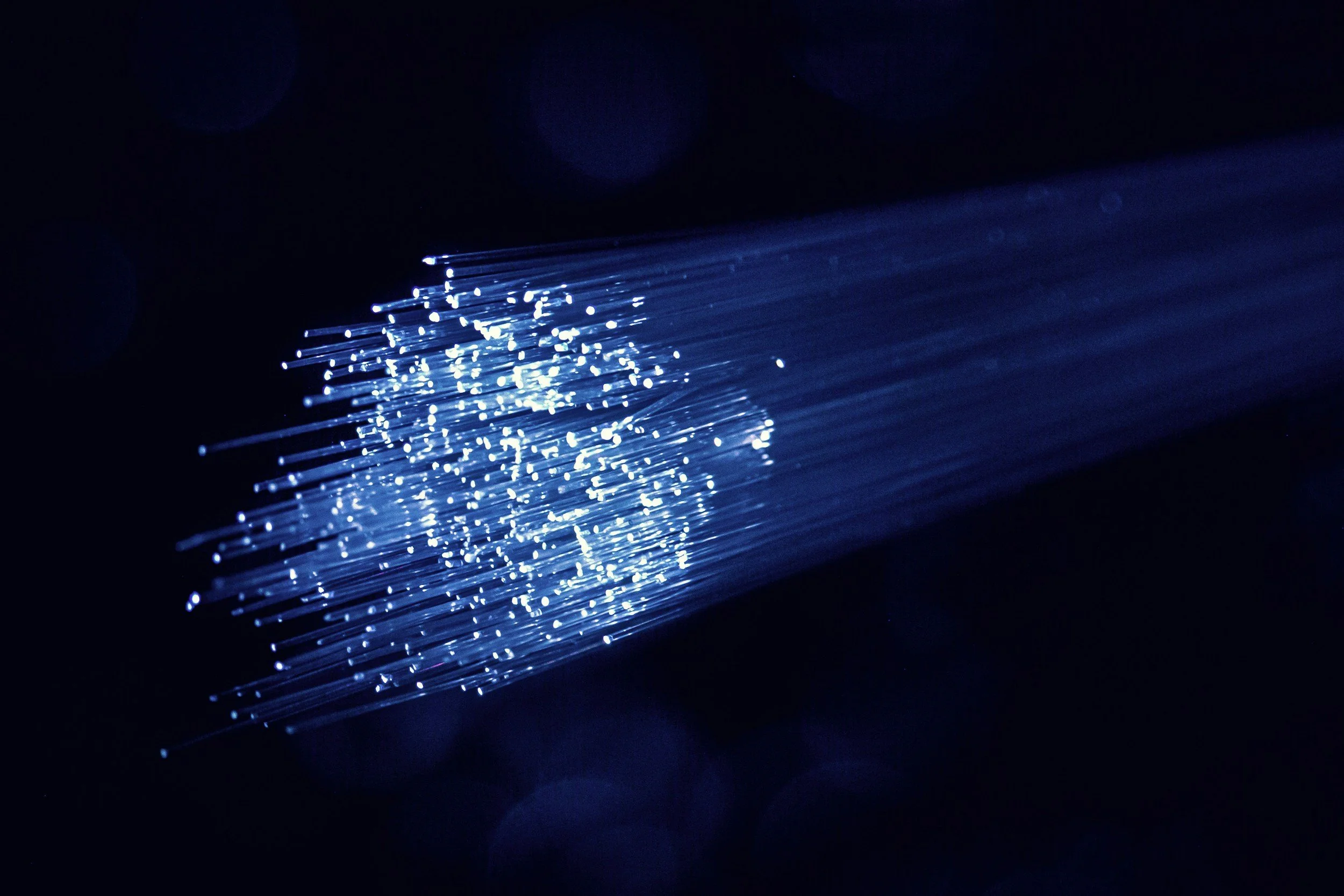 Close-up of fiber optic cables emitting blue light in a dark environment.