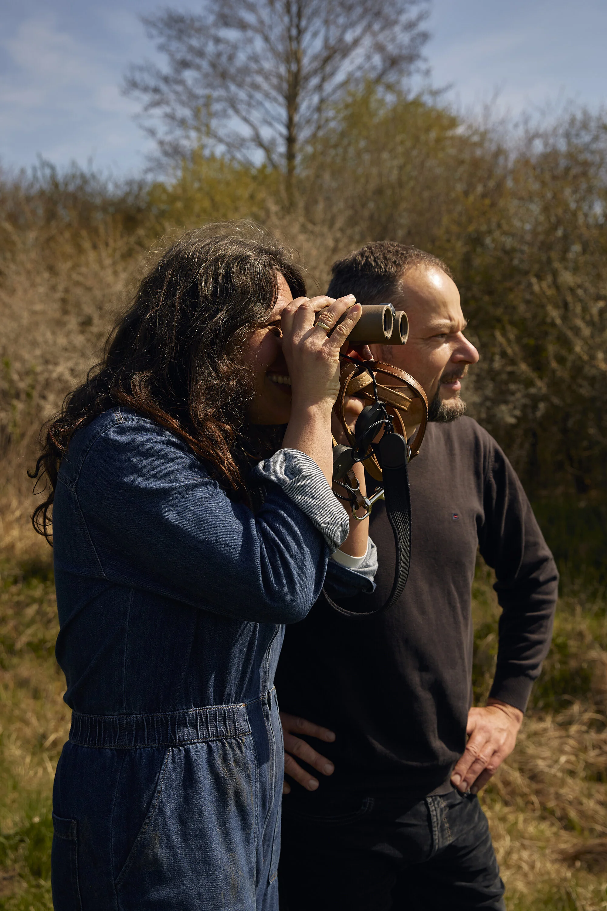 Ein Mann und eine Frau stehen in der Natur. Die Frau hält ein Fernglas.