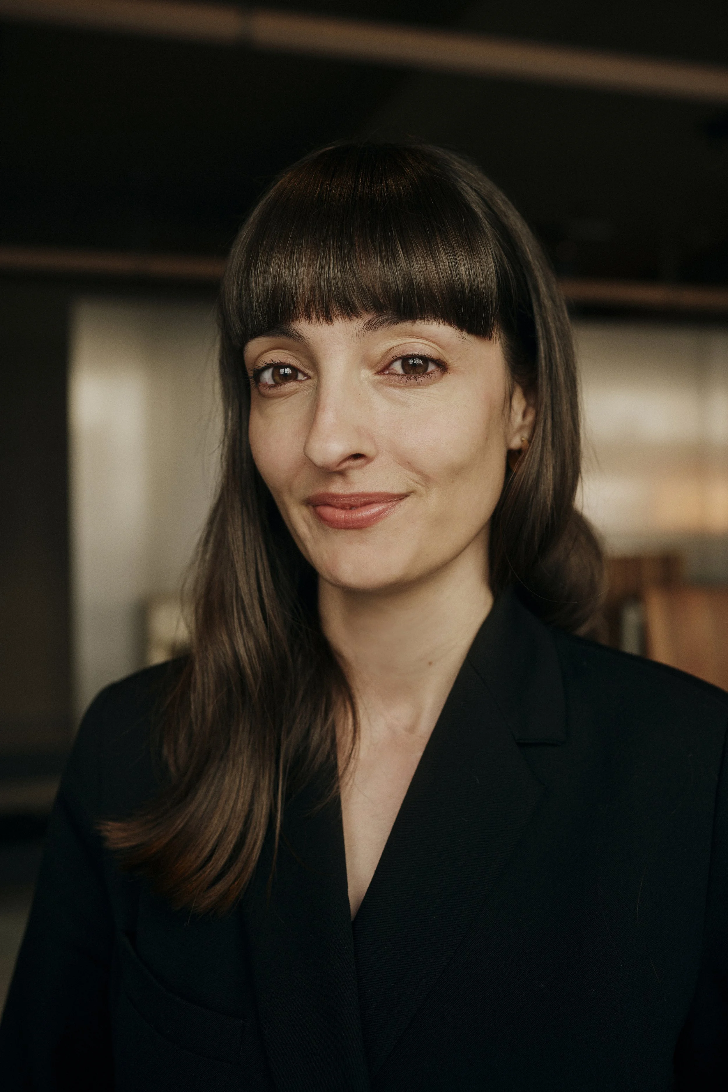 Porträt einer Frau mit langen braunen Haaren und Pony in einem schwarzen Blazer.