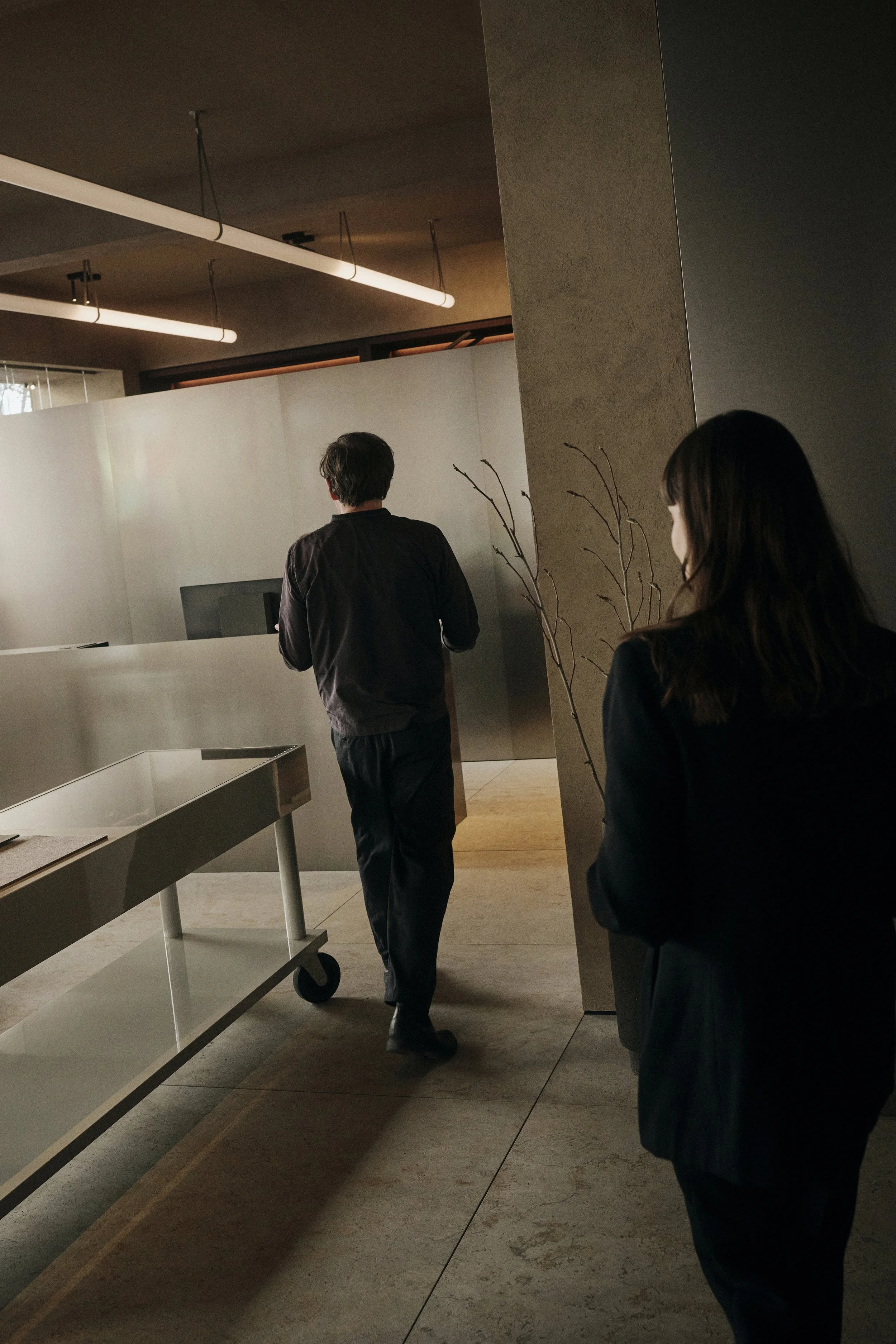 Zwei Personen laufen in einem modernen Büro mit Glaswänden und Deckenbeleuchtung.