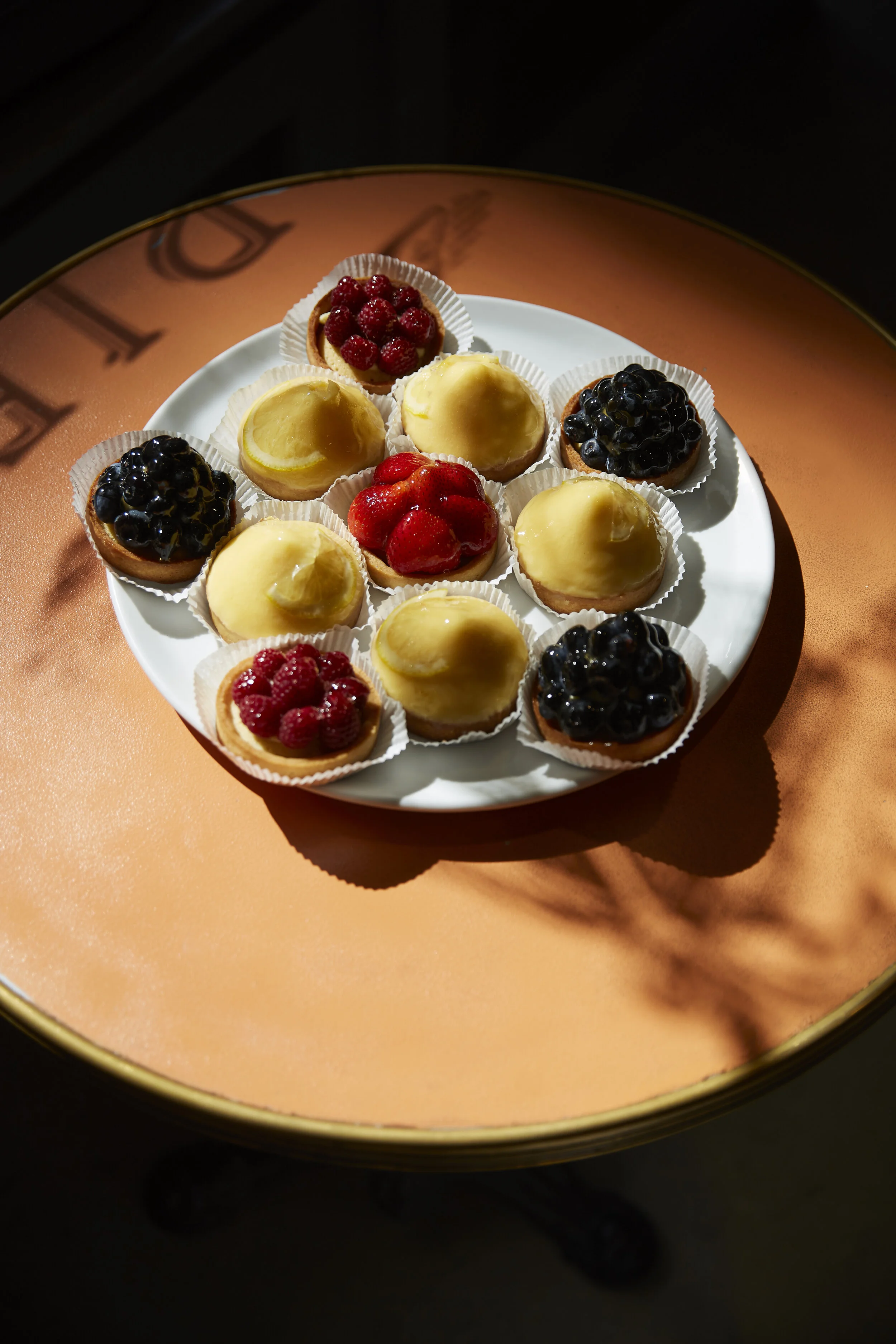 Törtchen mit verschiedenen Früchten, darunter Erdbeeren, Himbeeren und Blaubeeren, auf einem weißen Teller serviert.