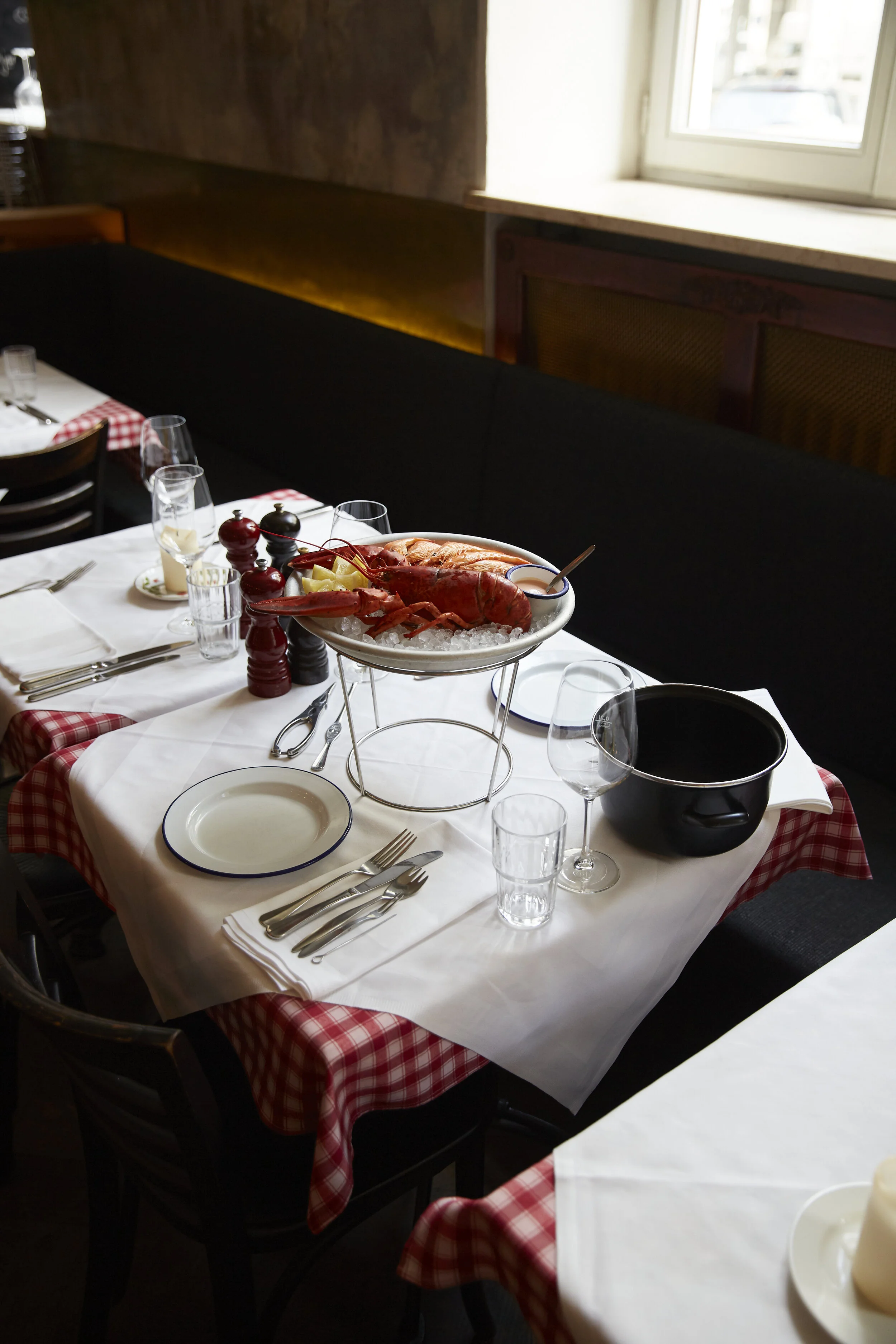 Ein gedeckter Tisch in einem Restaurant mit einem Tablett voller Meeresfrüchte, darunter Hummer, auf Eis serviert, umgeben von Besteck, Gläsern und einer Schüssel.