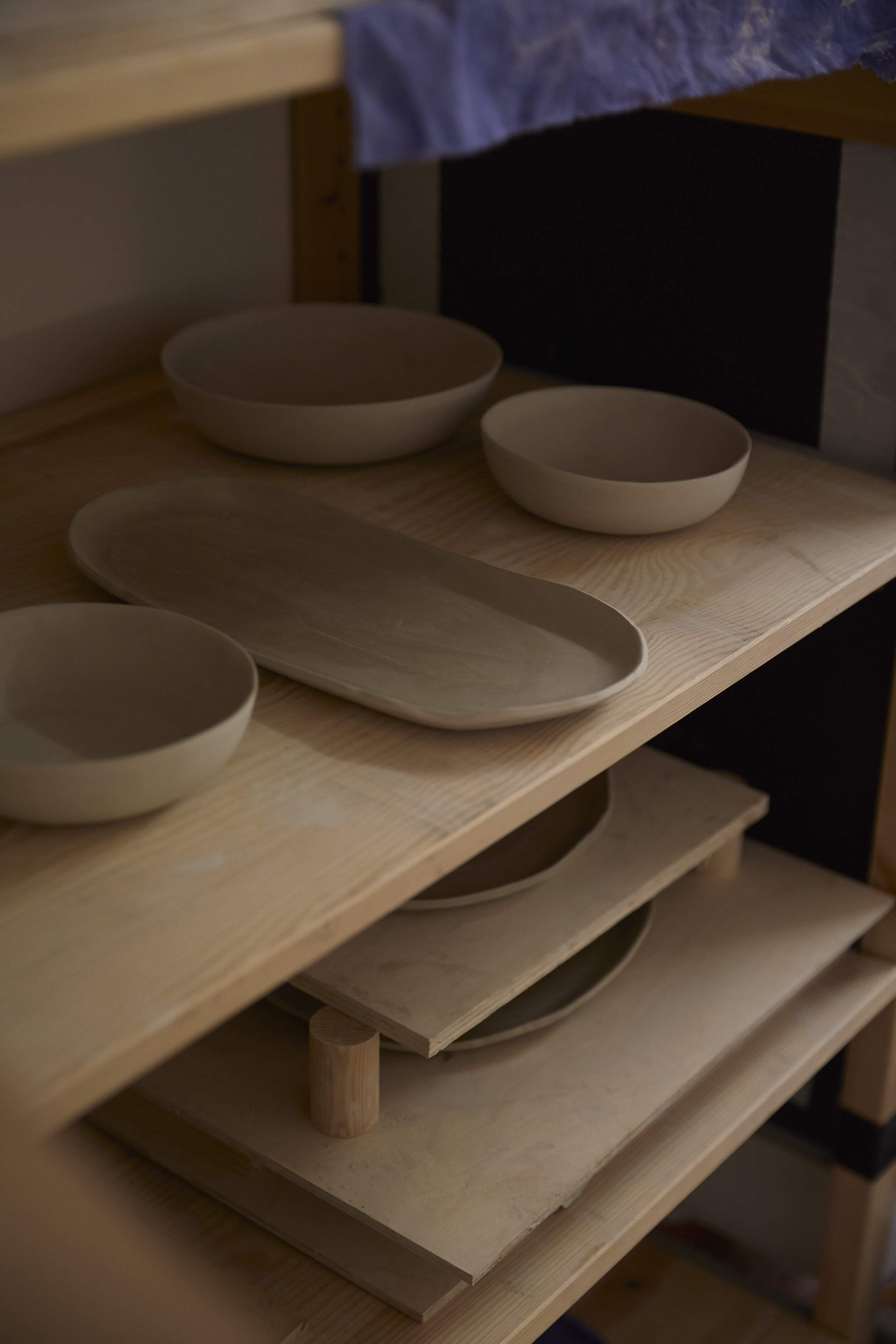 Keramikgeschirr, wie Schalen und Teller, auf einem Holzregal gestapelt.