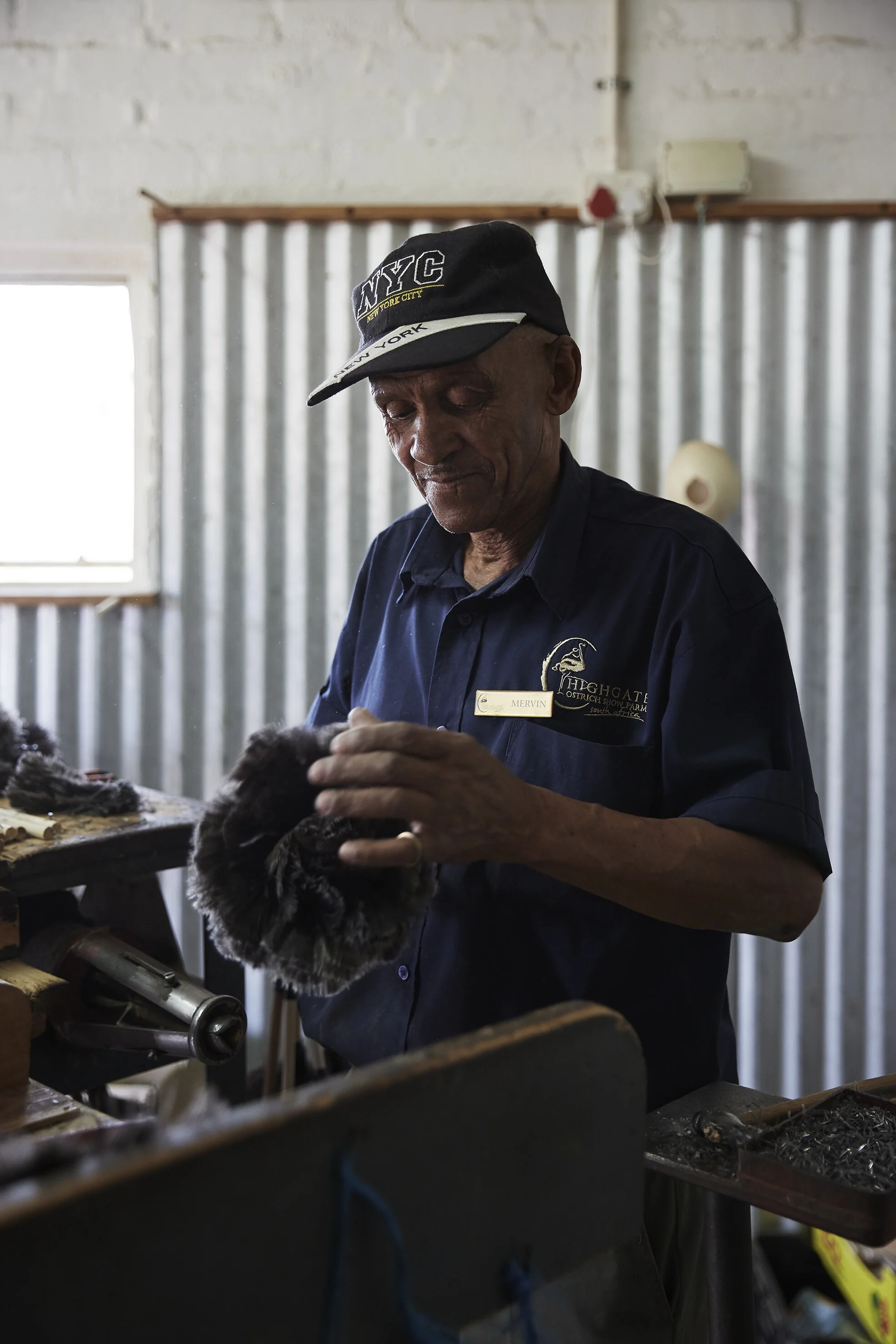 Älterer Mann mit Baseballkappe in Werkstatt, hält ein Fellstück in der Hand.