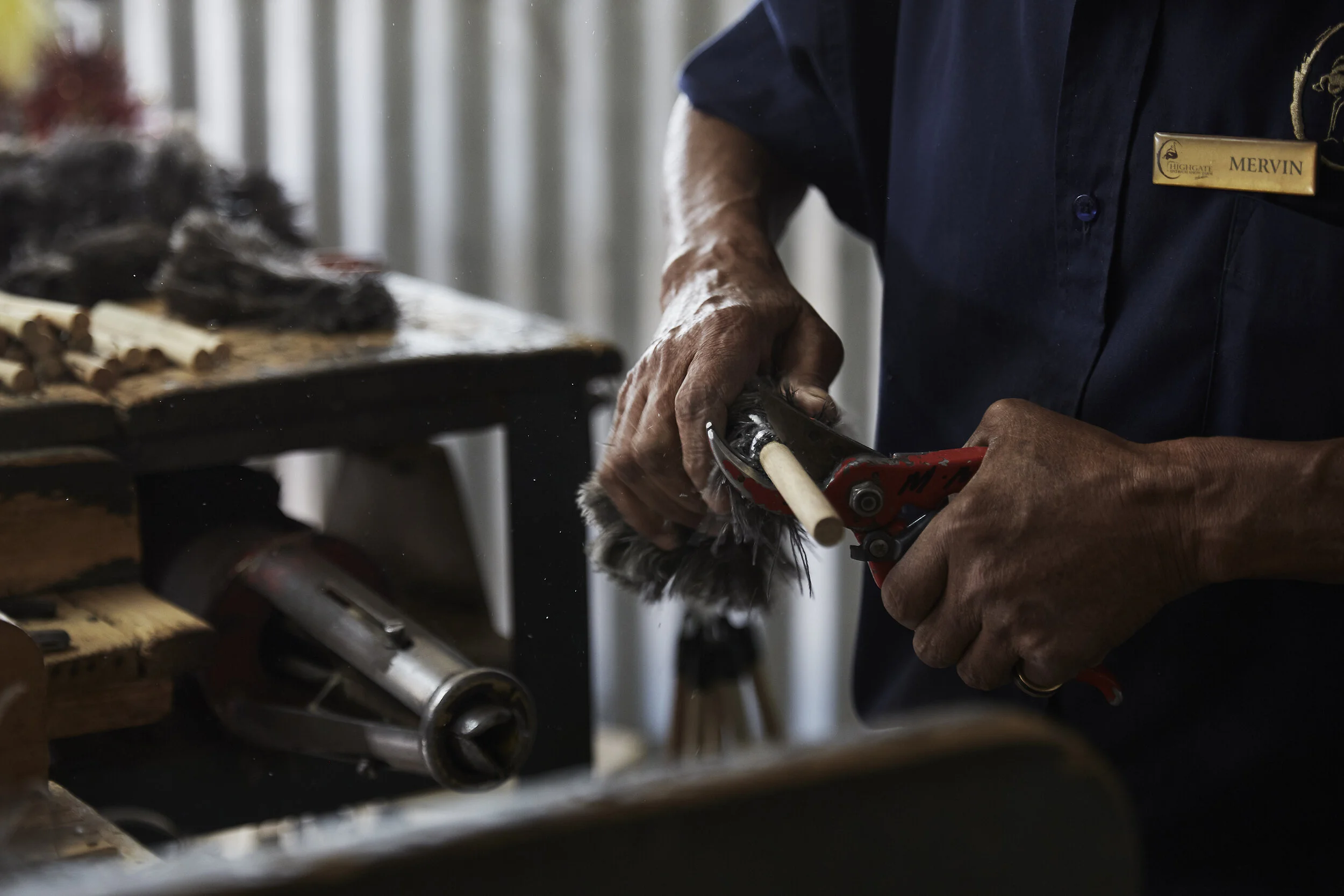 Person, die an einem Holzstab mit einem Werkzeug arbeitet, in einer Werkstattumgebung.