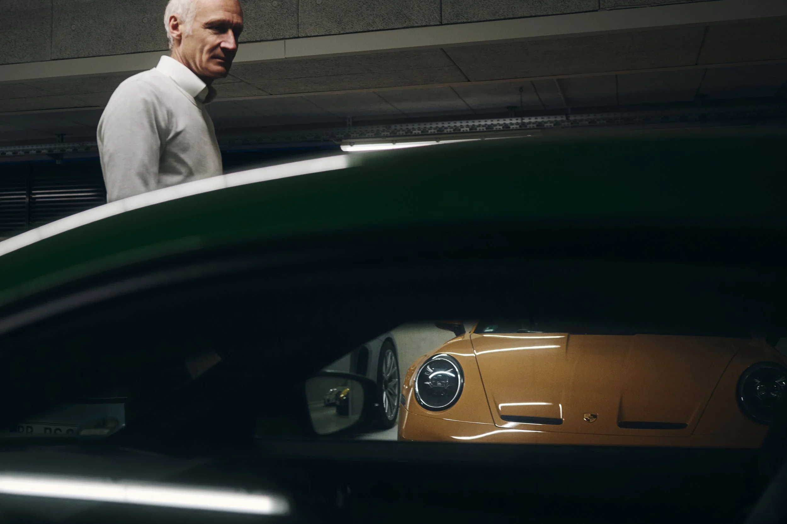 Ein Mann in einem Parkhaus steht neben einem grünen Auto. Im Hintergrund ist ein gelbes Auto, vermutlich ein Porsche, zu sehen.
