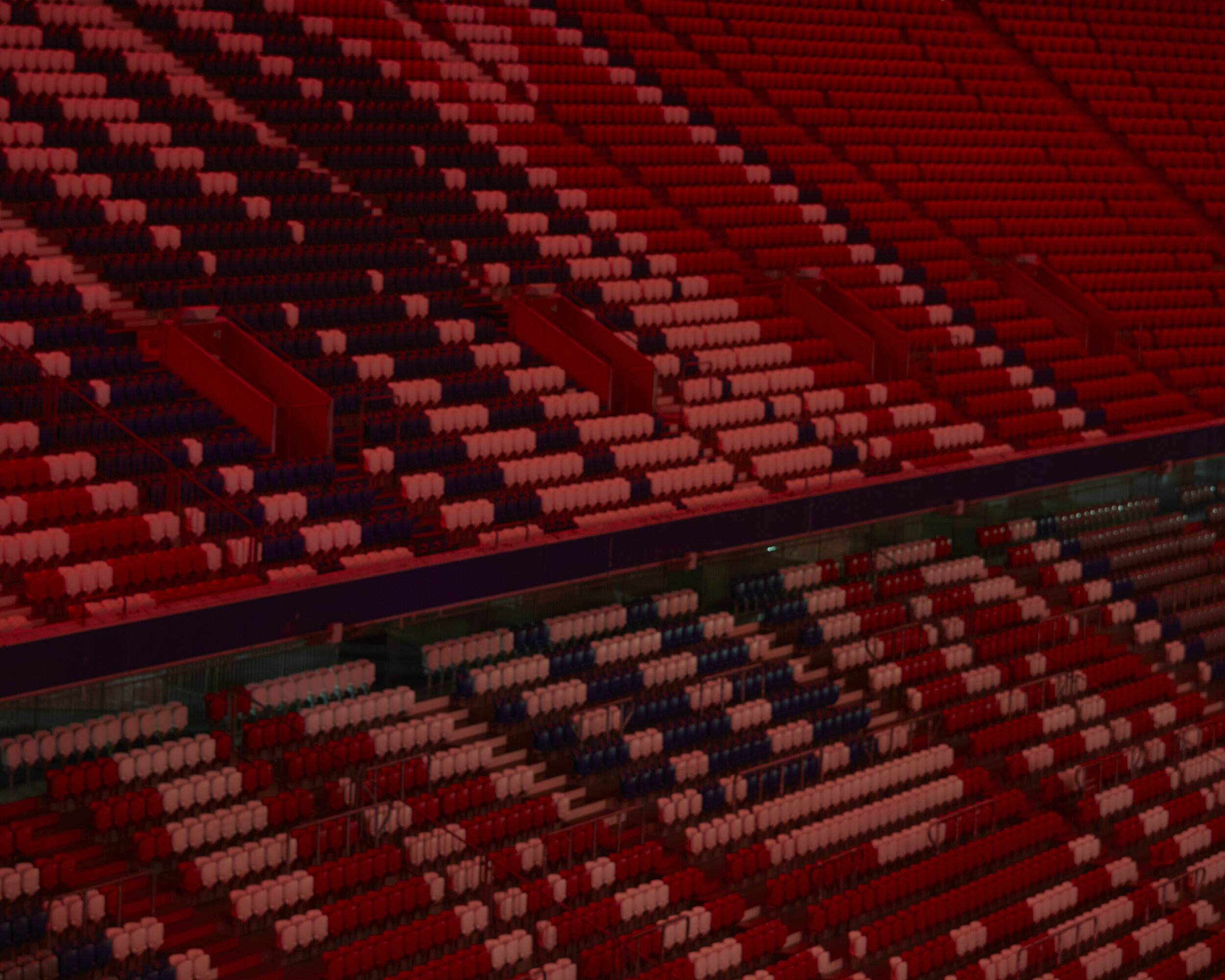 Leere Stadiontribünen mit rot-weiß-blauen Sitzen, die ein Muster bilden.
