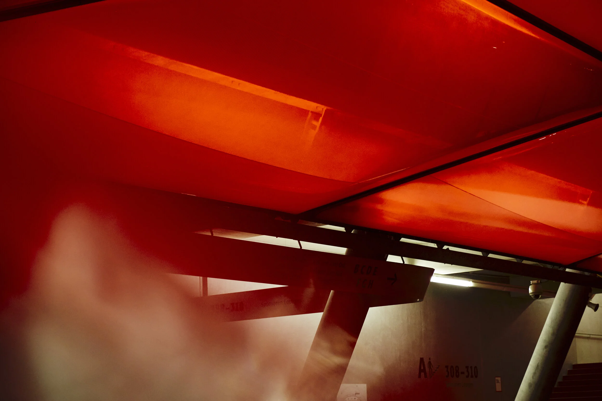 Innenansicht einer modernen Architekturstruktur mit rotem Dach und Nebel. Wände und Stützbalken sind sichtbar.