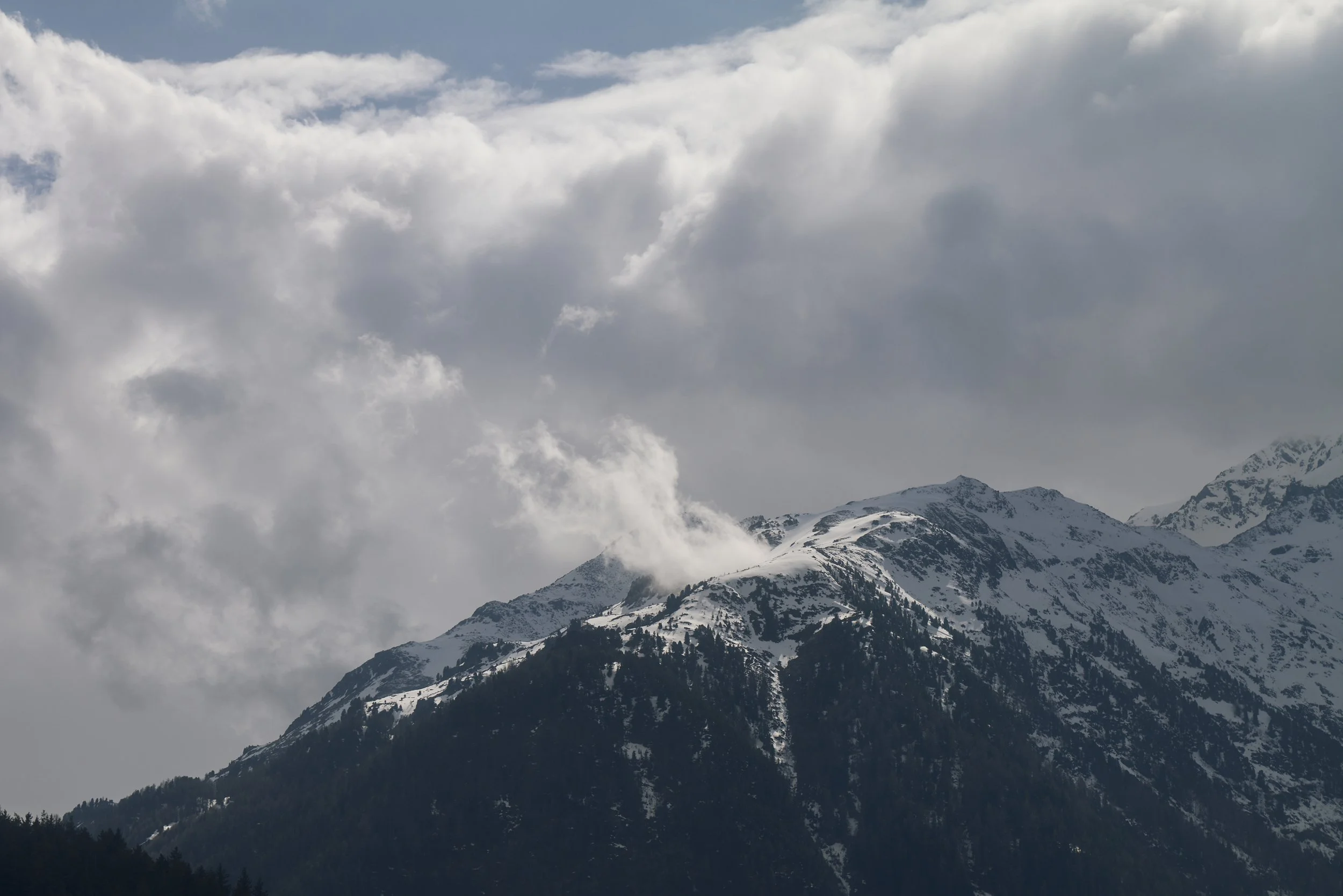 Schneebedeckte Berggipfel unter bewölktem Himmel mit dichten Wolken in den Alpen.