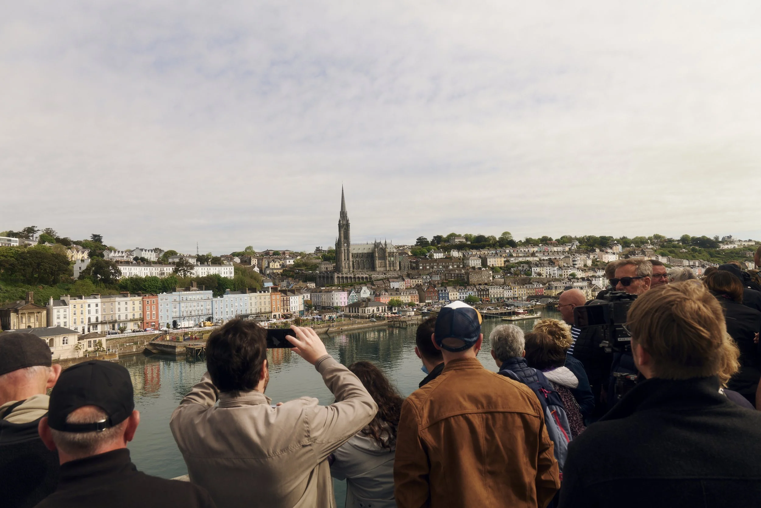 Menschen beobachten ein malerisches Küstendorf mit einer Kirche und bunten Häusern.